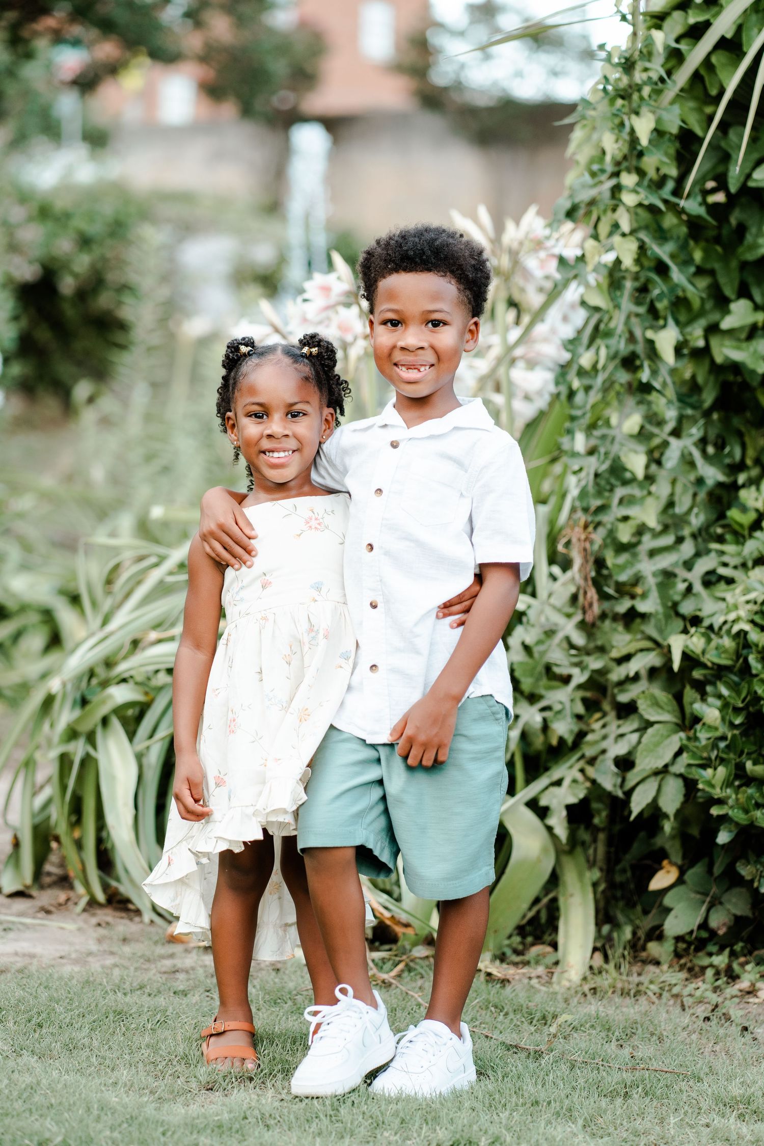 Two children in coordinating white and mint green outfits pose playfully in a garden setting.