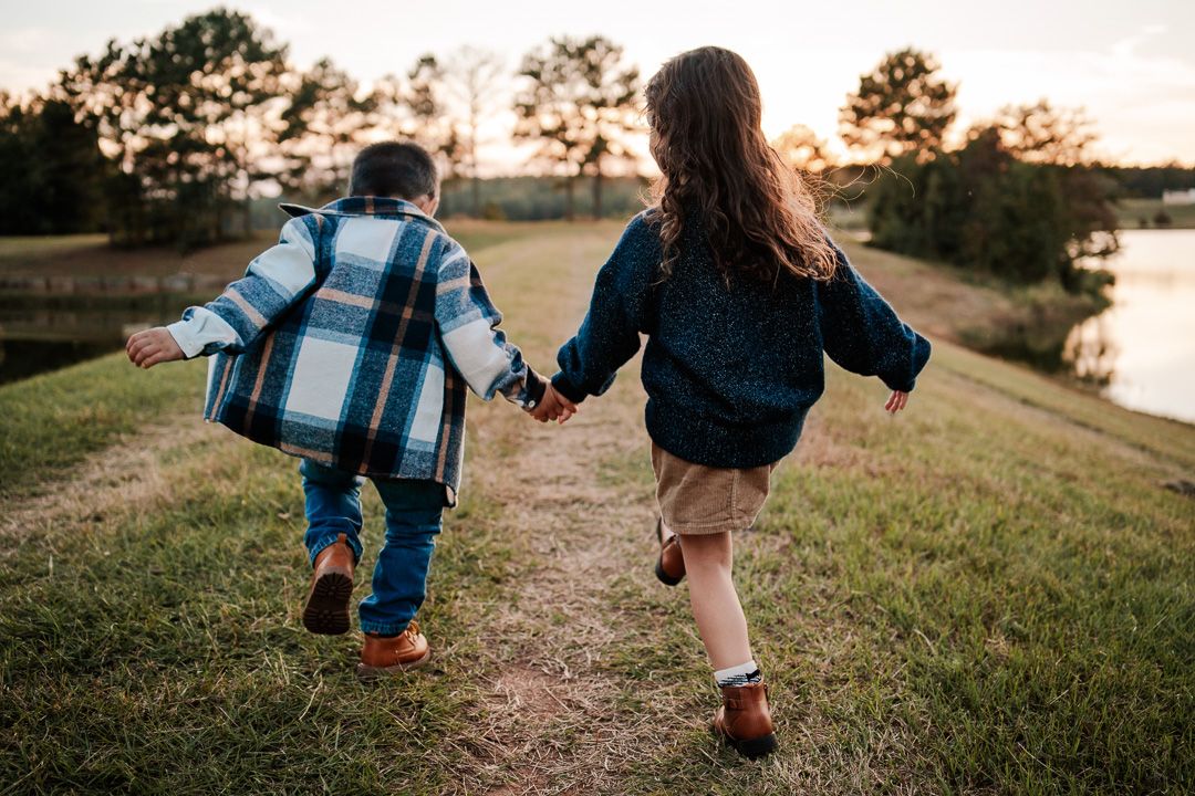 Playful family running together on grassy path during golden hour.