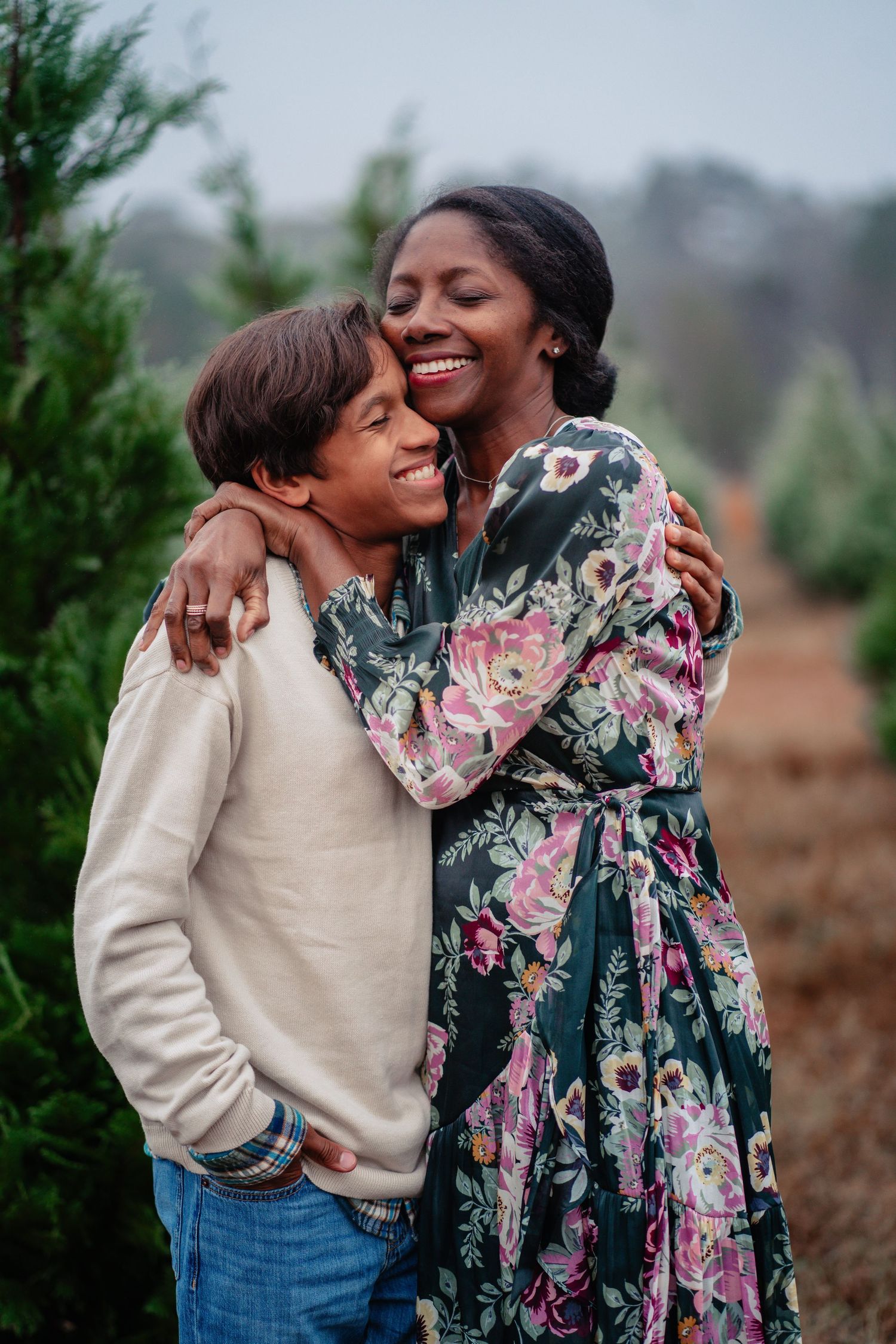 Two people share a joyful embrace outdoors, one wearing a floral dress and the other in a cream sweater and jeans.