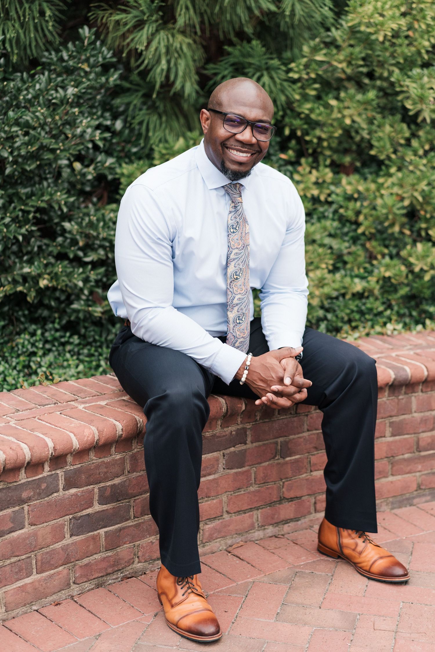 Person in business attire sitting on brick wall wearing brown leather shoes.