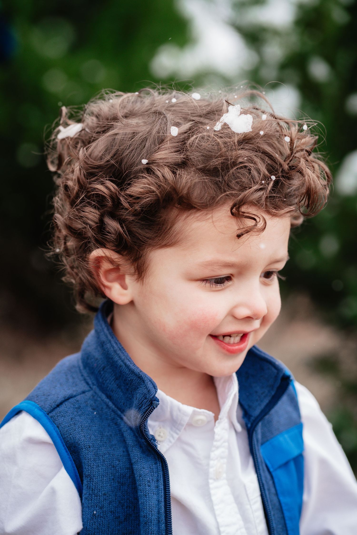 A series of candid profile shots showing a child with curly hair wearing a blue vest and white shirt smiling and laughing.