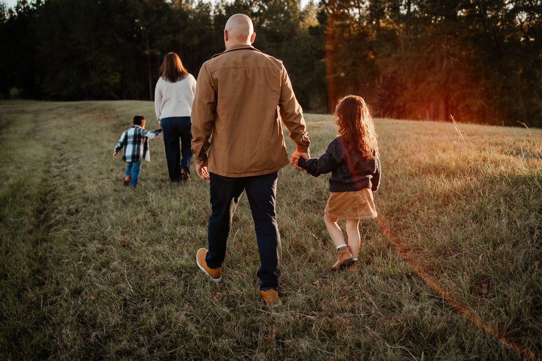 Family walking together on a path during sunset with tall trees in the background.