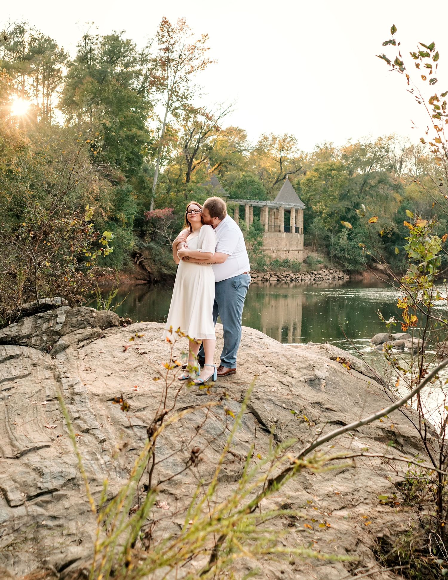 Scenic engagement photos on rocky landscape with lake and gazebo during sunset.
