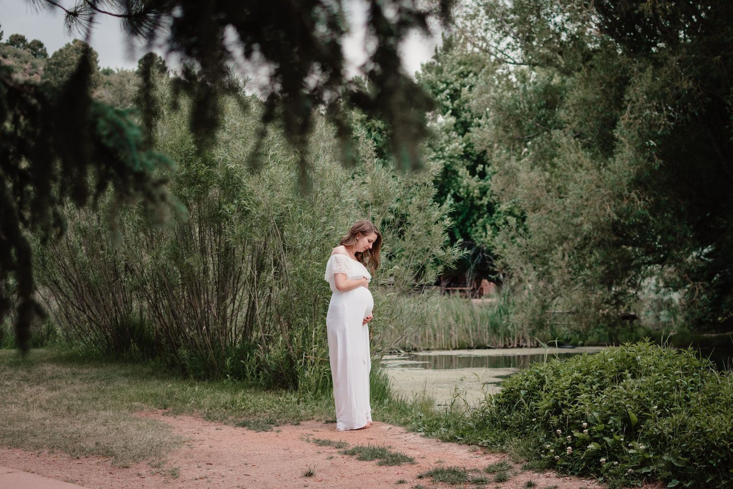 A person in a flowing white dress poses gracefully in a lush green outdoor garden setting.