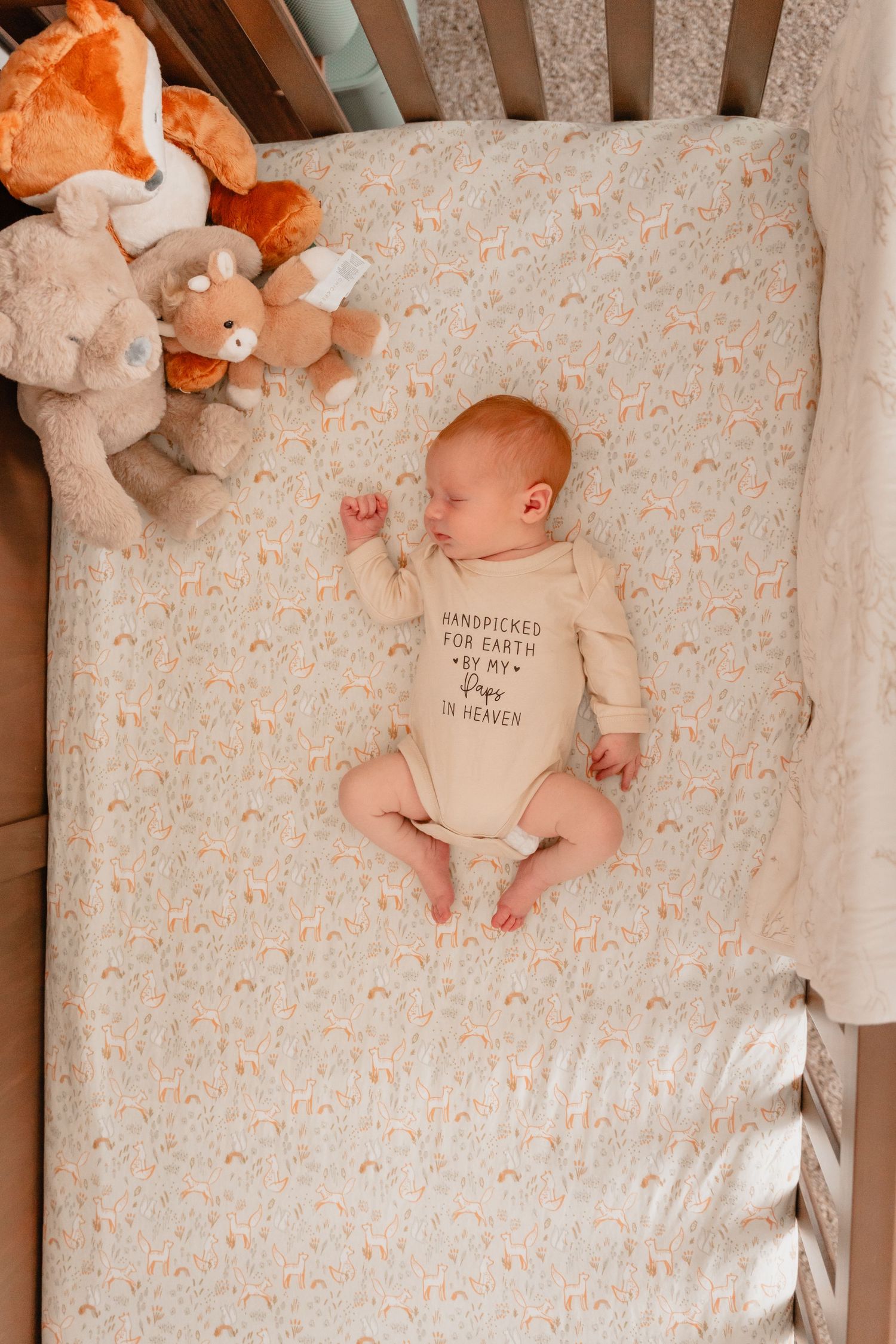 Newborn baby in a cream onesie reading 'Handpicked for Earth by my Angel in Heaven' lying in a crib.