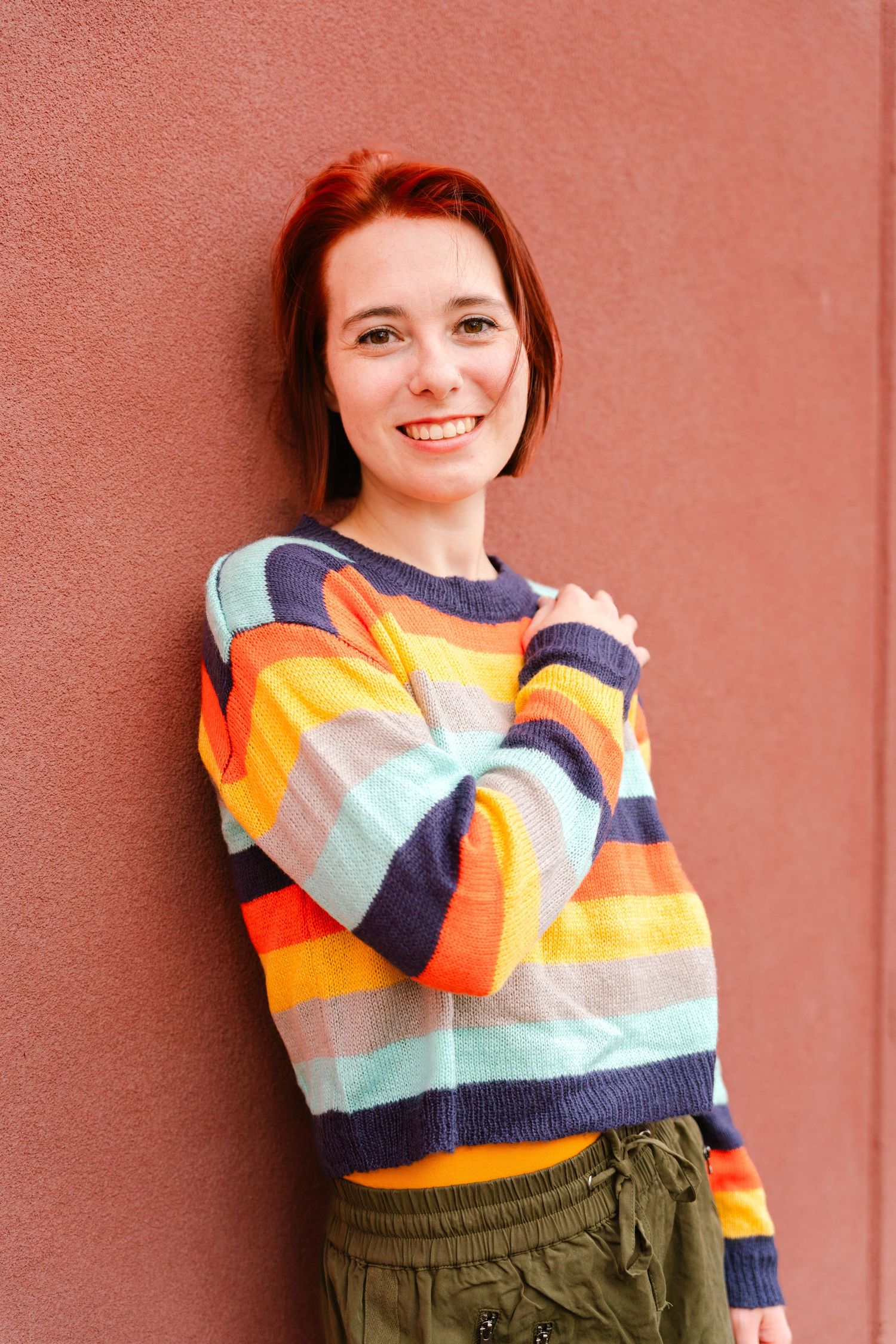 Colorful striped sweater with bright orange and teal pattern against coral wall.