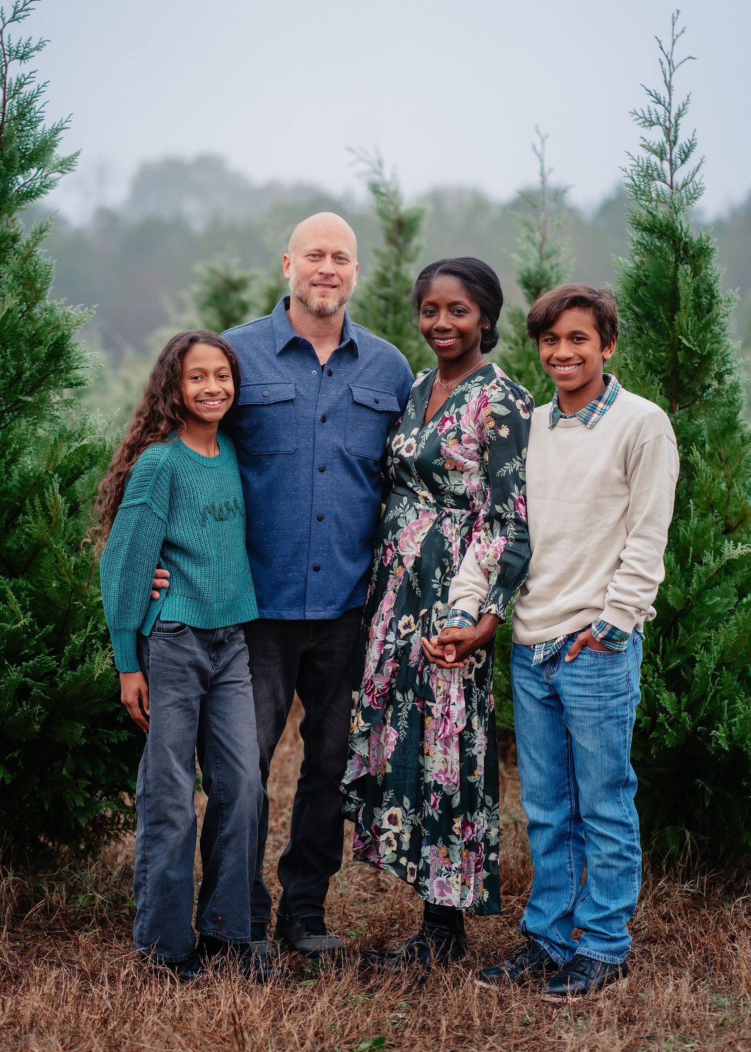 A group of people pose together outdoors near evergreen trees on a misty winter day.
