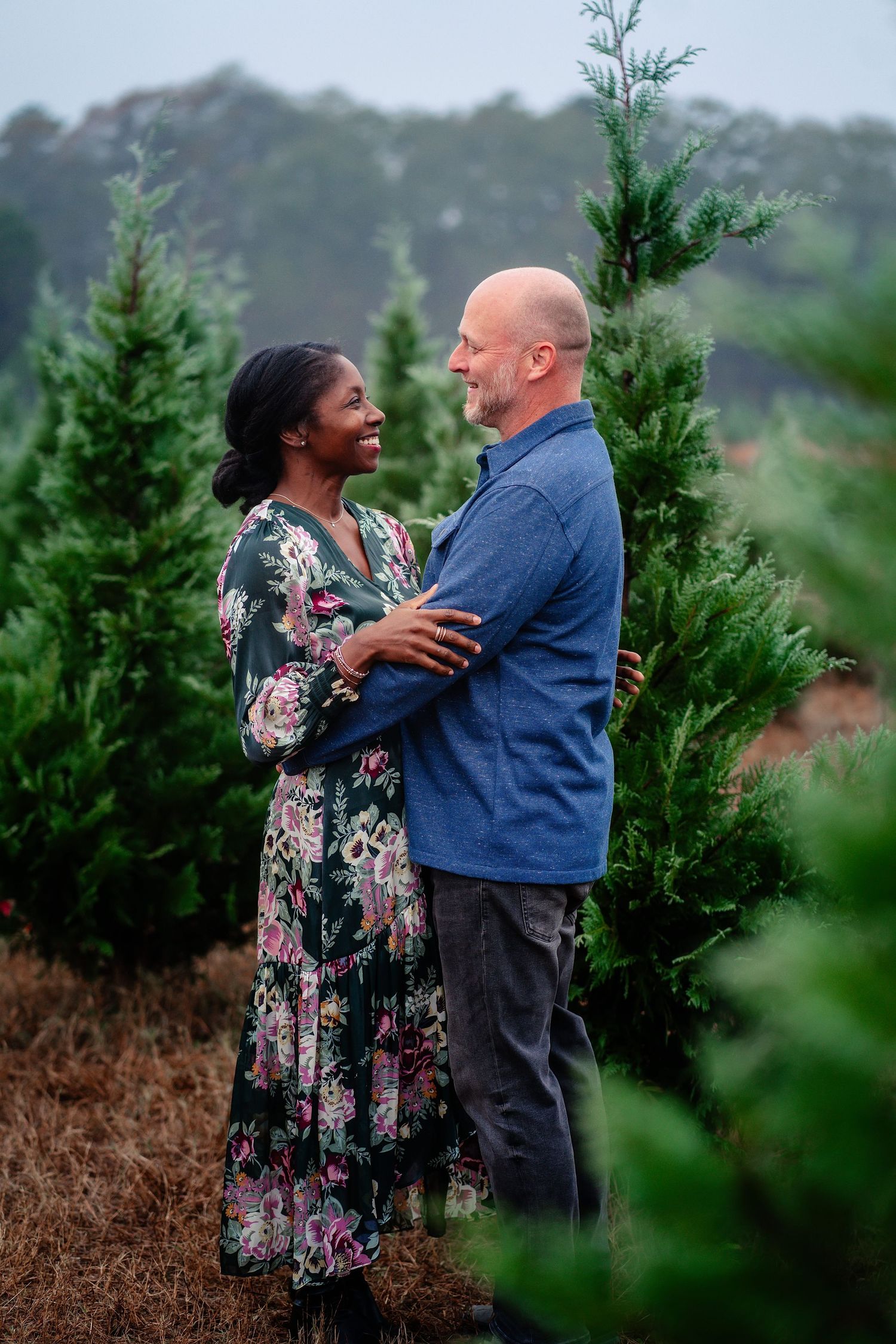 A couple shares a romantic moment together among evergreen trees in a misty outdoor setting.