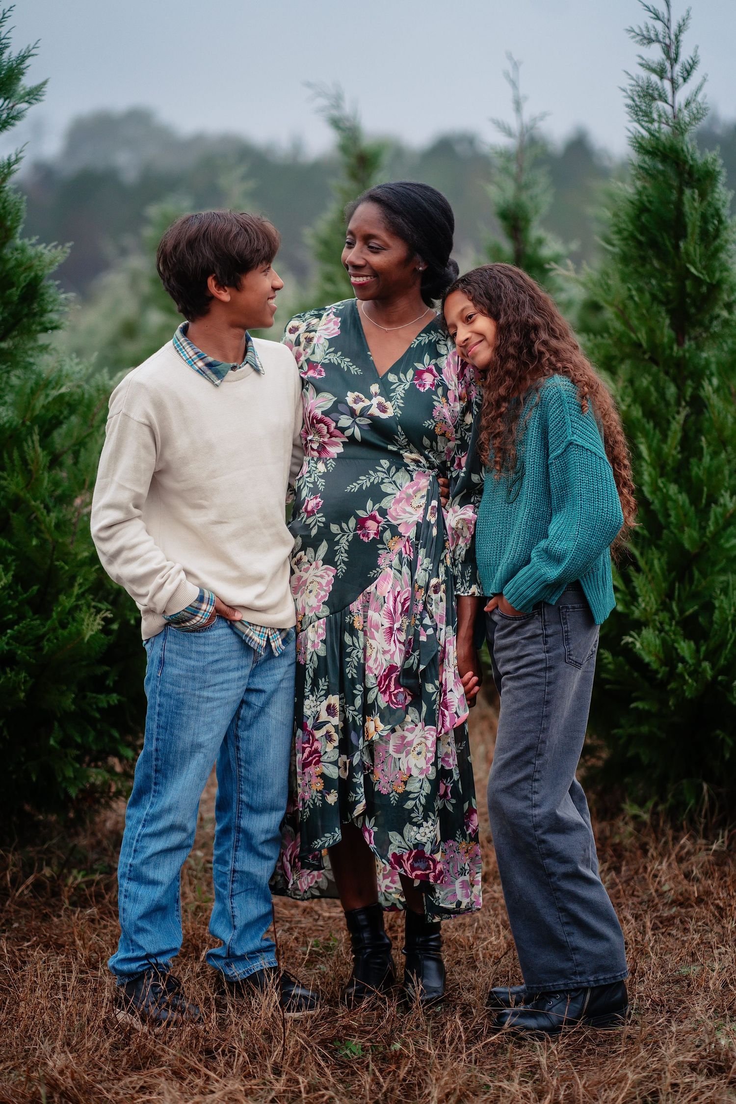 Three people share joyful moments together while standing among evergreen trees on a misty day.