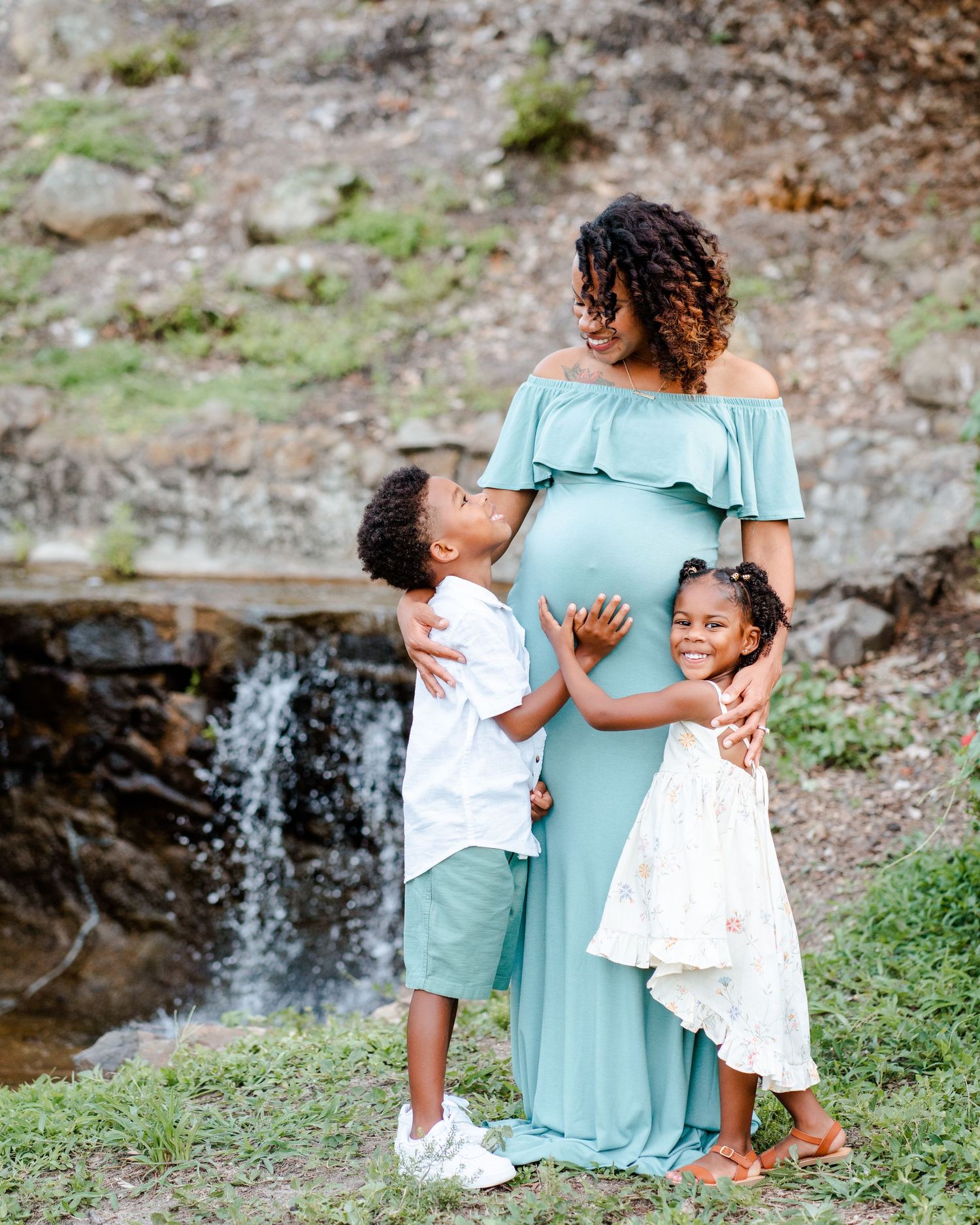 A family shares tender moments near a scenic waterfall, wearing coordinating mint green and white outfits.