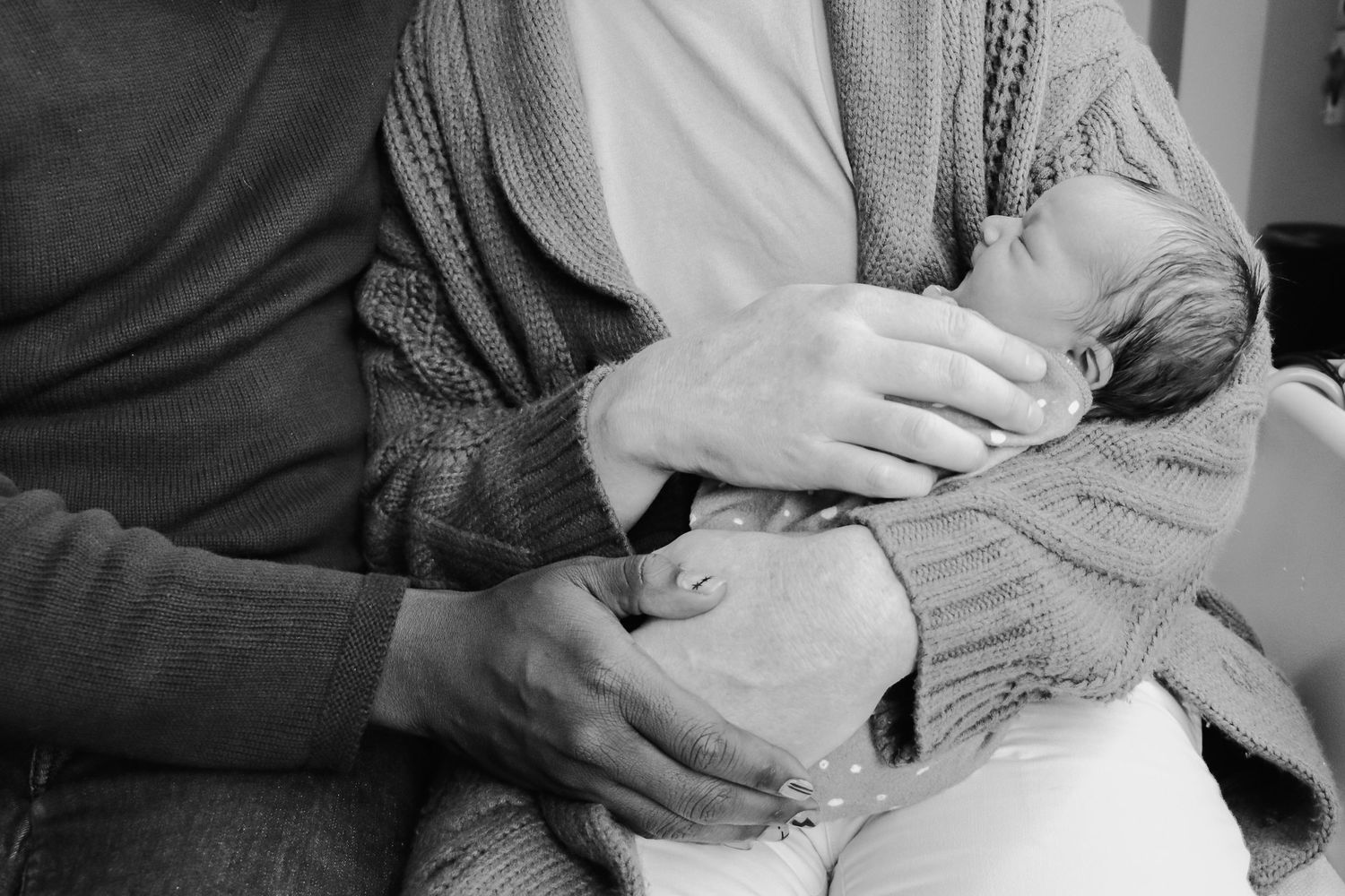 Black and white image of sleeping infant being cradled in caregiver's arms.