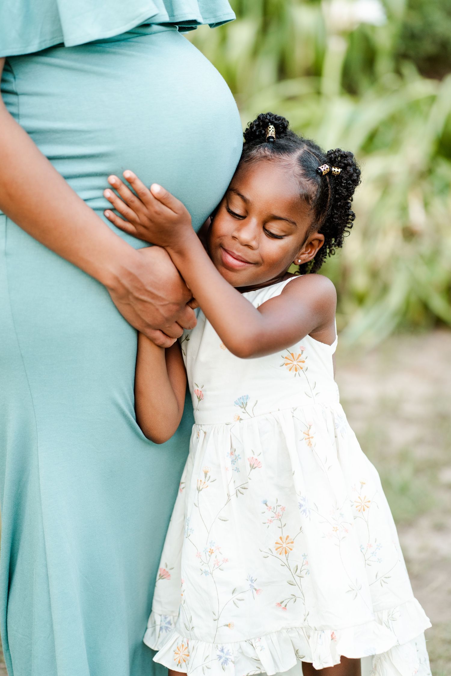 A series of tender moments captured between a person in a teal dress and a child in a white floral dress outdoors.