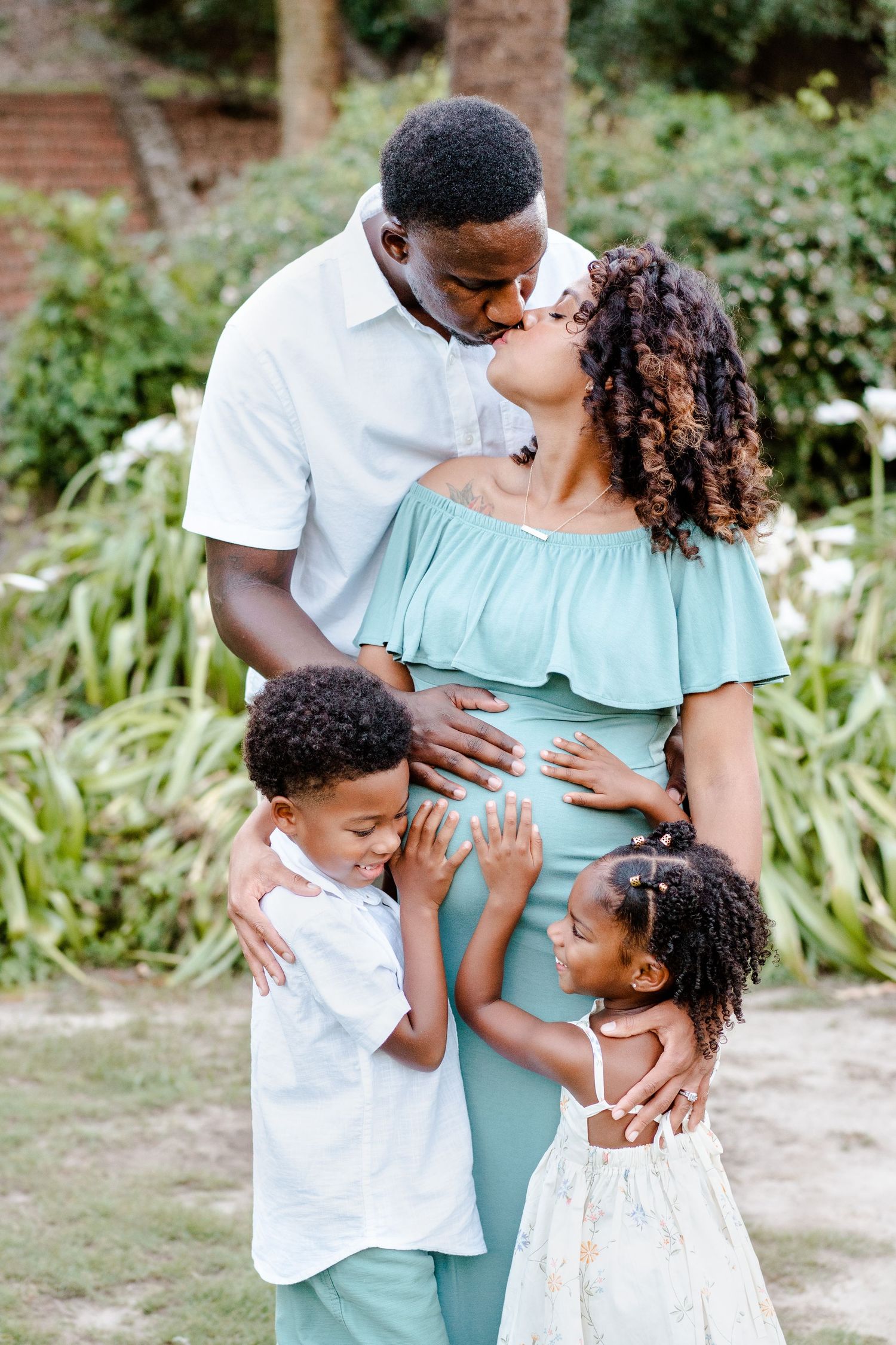 A loving family shares an intimate moment together in a garden setting, wearing coordinated white and mint green outfits.