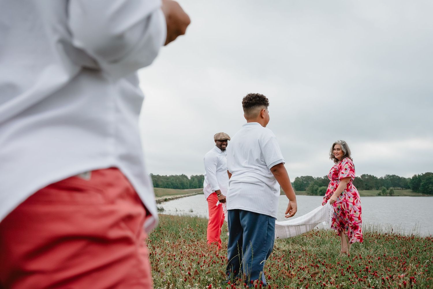 Family running through a vibrant red flower field under cloudy skies.