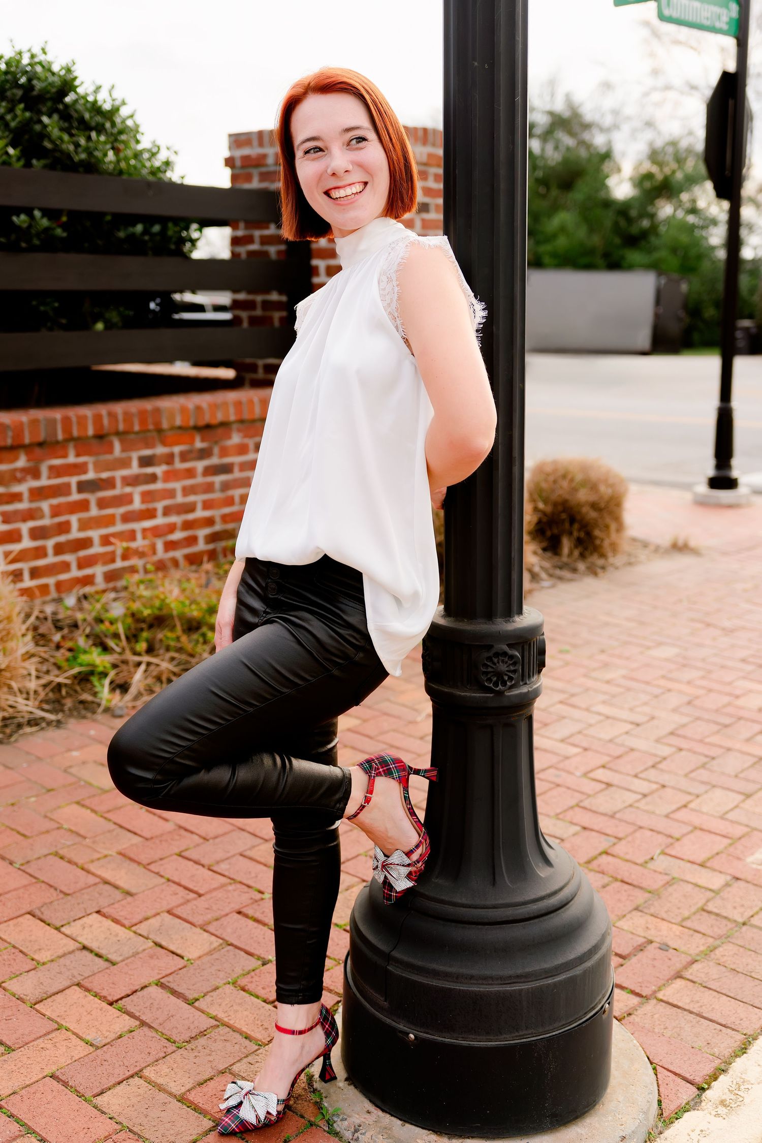 Person in business attire sitting on decorative black lamp post on brick patio.
