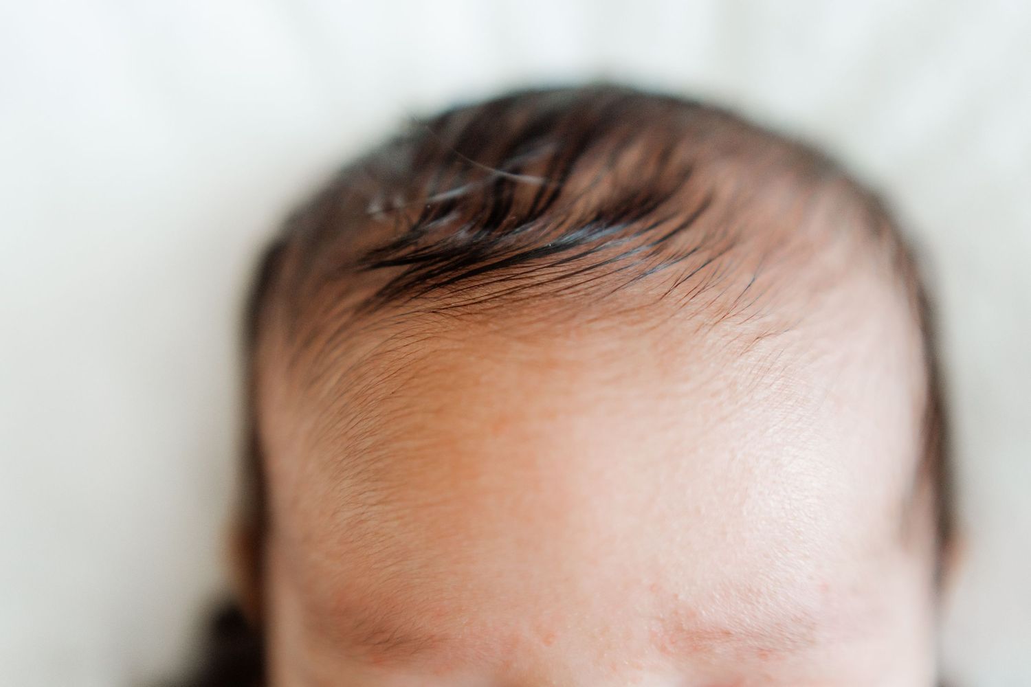Close-up view of a sleeping newborn's forehead and dark hair.