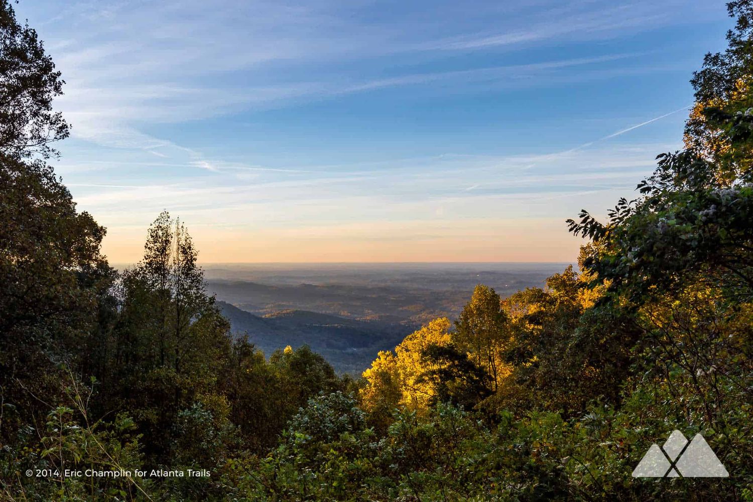 Panoramic autumn mountain vista with colorful foliage framing a sweeping valley view under a blue sky at golden hour.