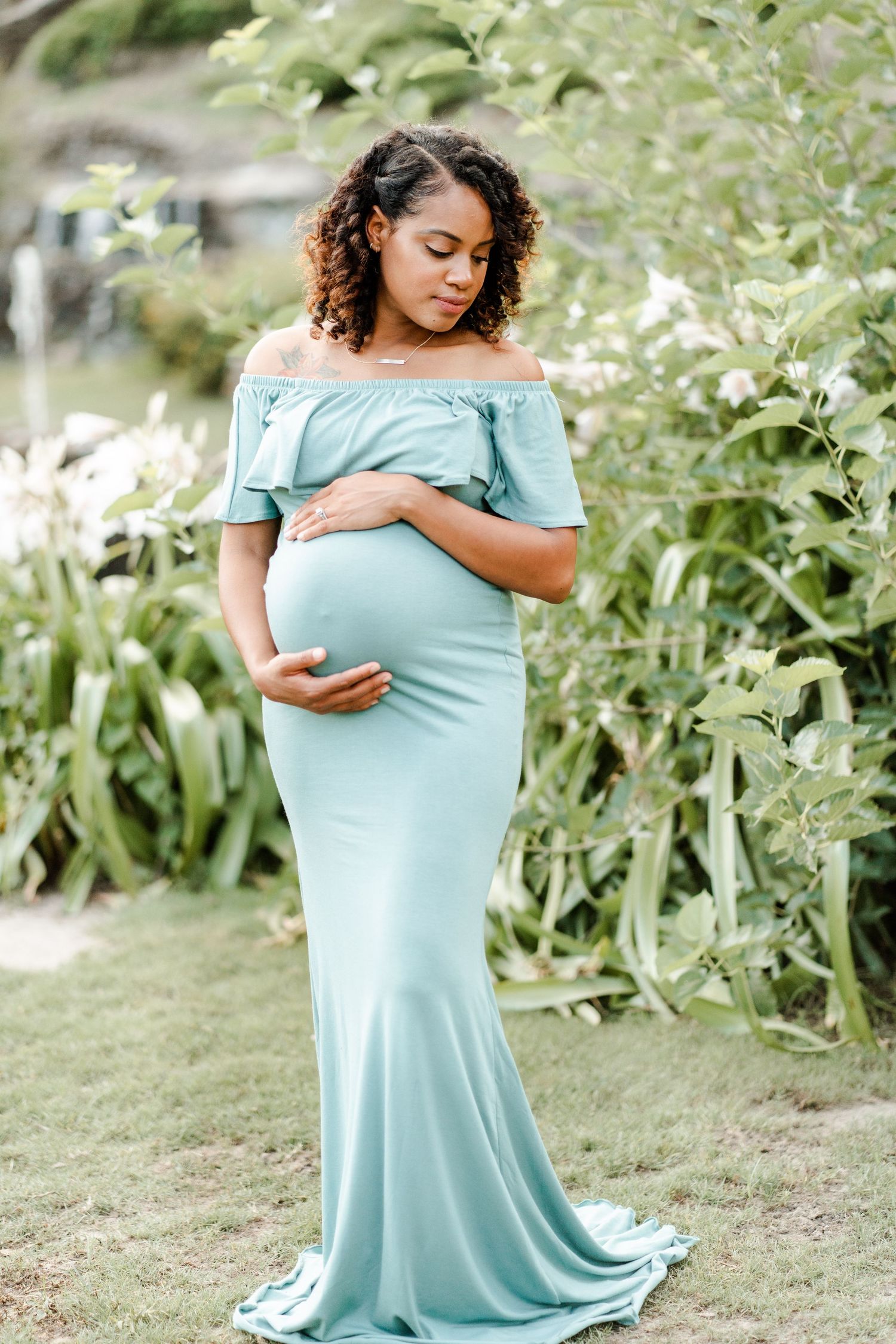 A person in a light turquoise off-shoulder dress poses gracefully in a garden setting with white flowers in the background.