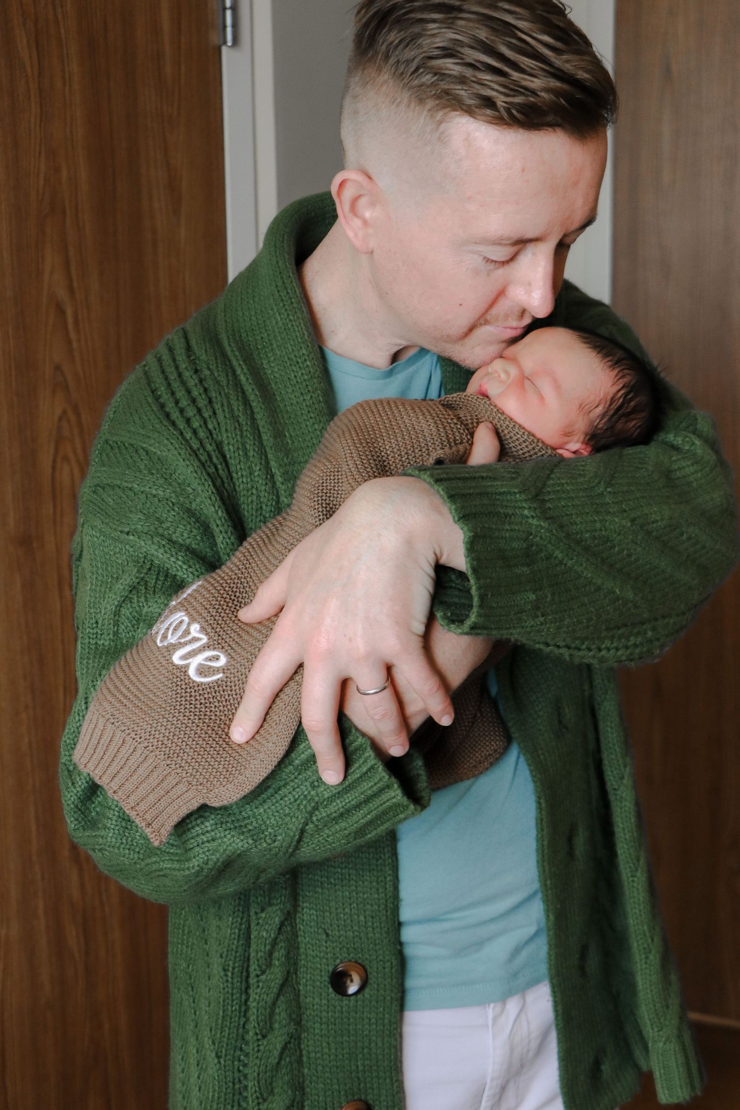 A tender moment between parent and newborn baby, with the adult wearing a green cardigan sweater and holding the infant.