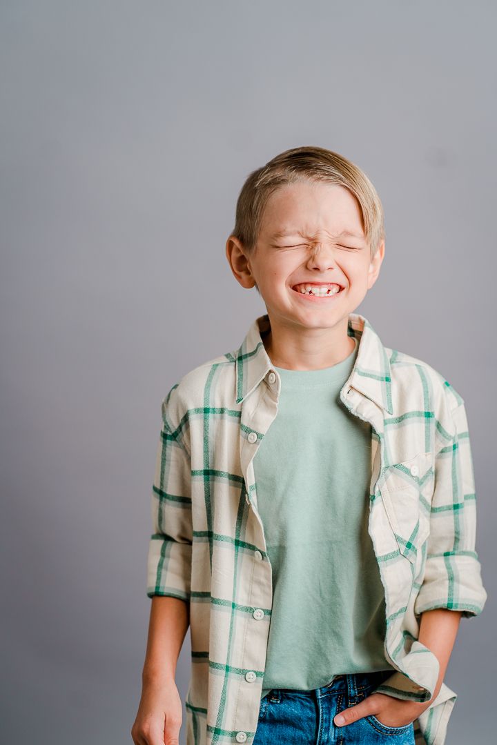 A child wearing a plaid button-down shirt and mint green t-shirt poses against a gray background.