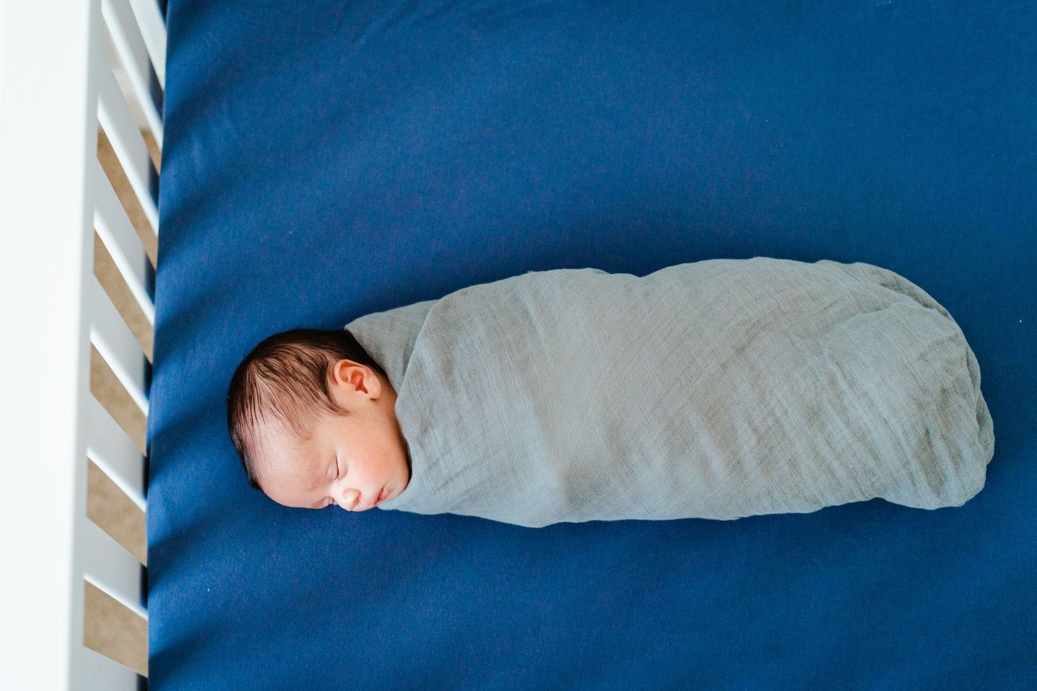 Swaddled newborn baby sleeping peacefully on blue bedding in a crib.
