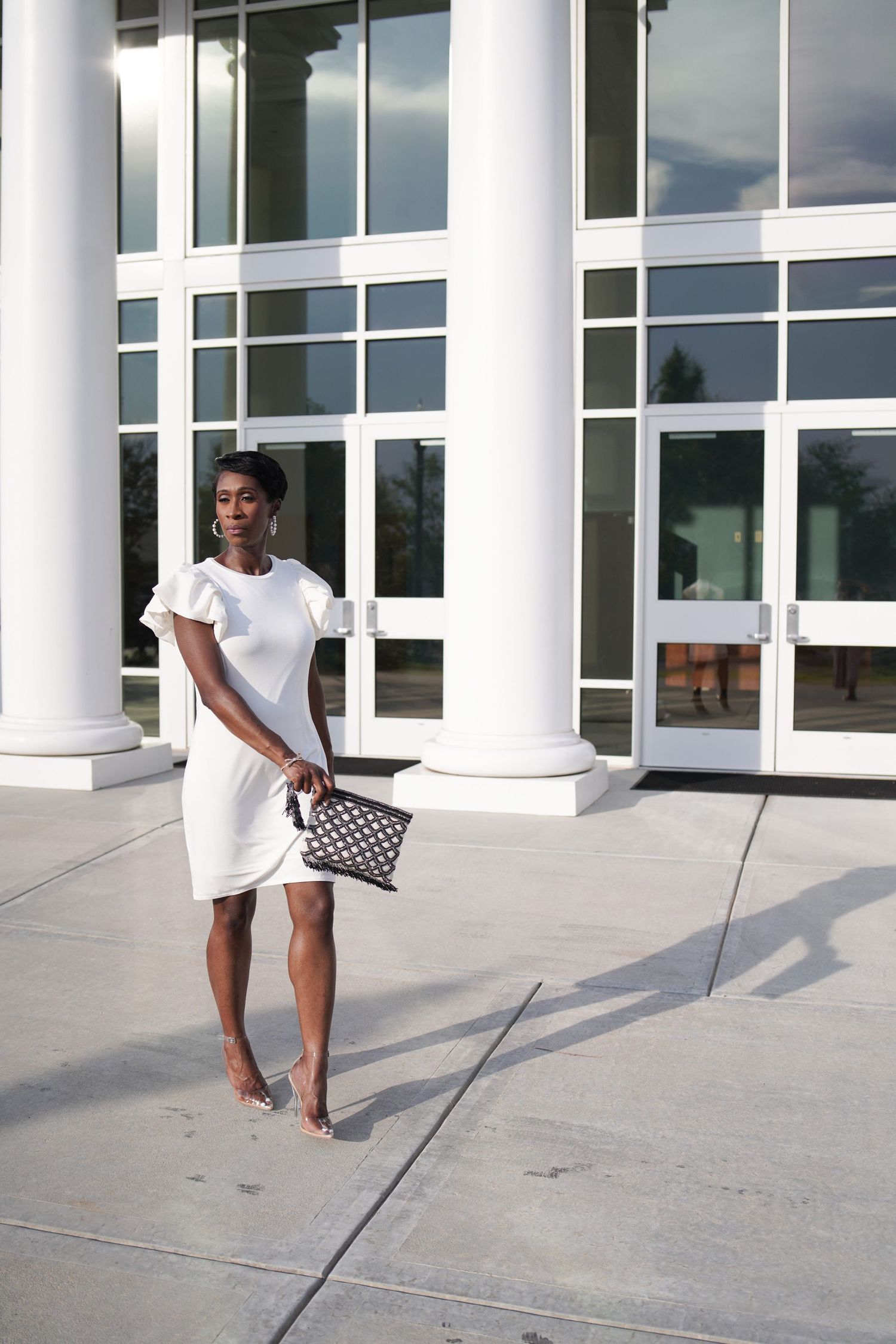 Stylish outdoor photoshoot featuring white dress and designer handbag against modern architecture.