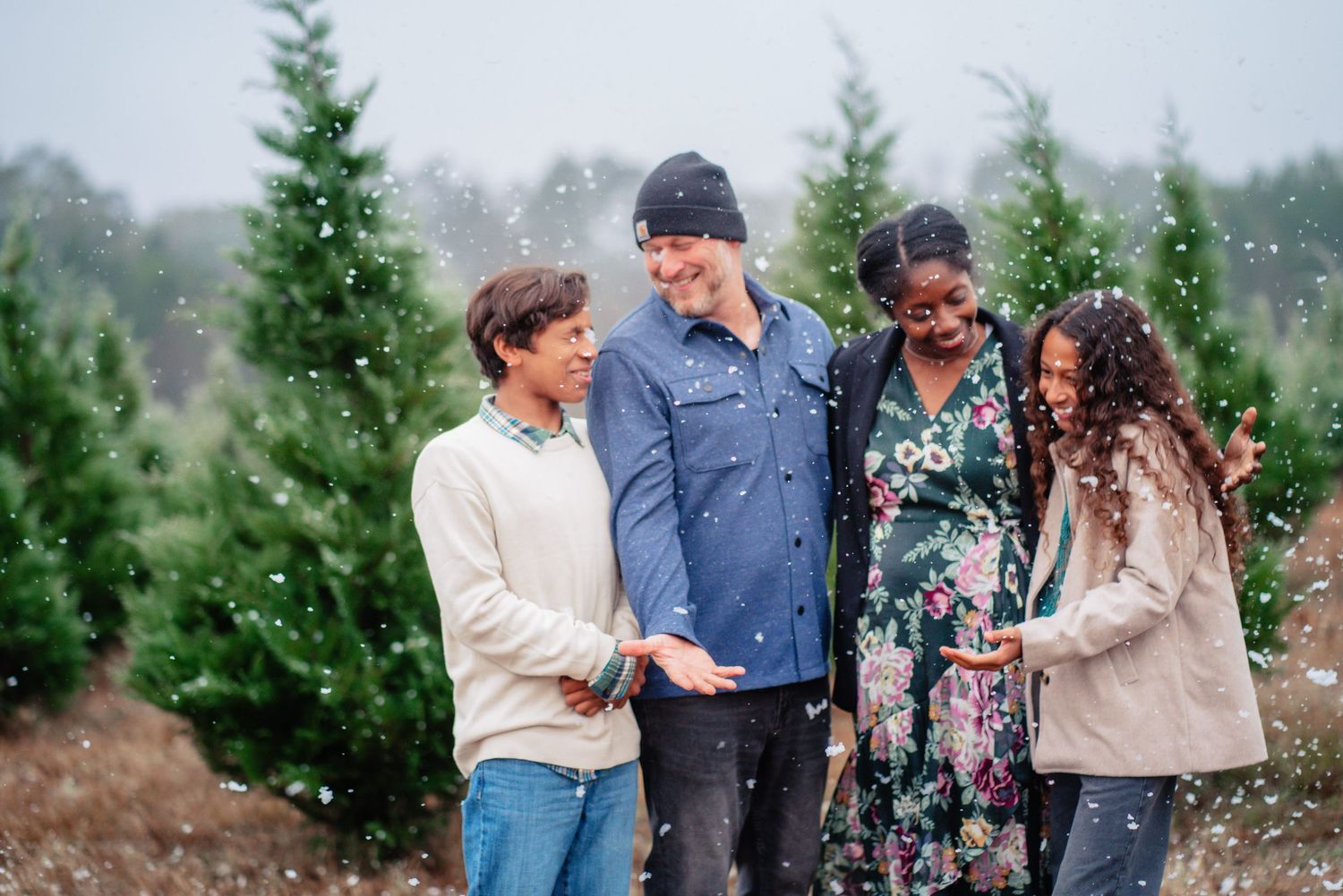 A group of people laugh and celebrate together in front of evergreen trees on a misty winter day.