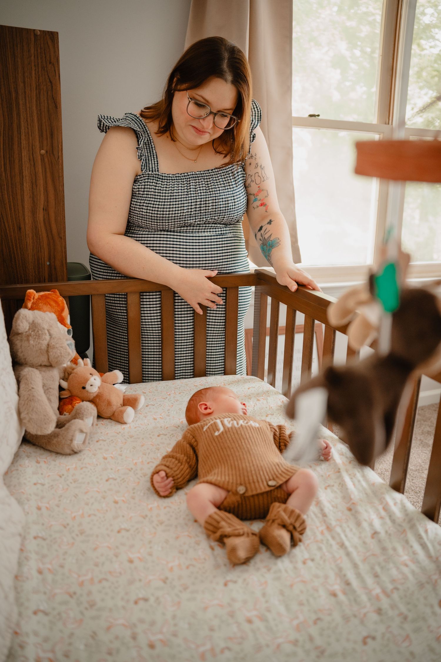 A mother gazes lovingly at her baby lying in a wooden crib surrounded by stuffed animals in a cozy nursery.