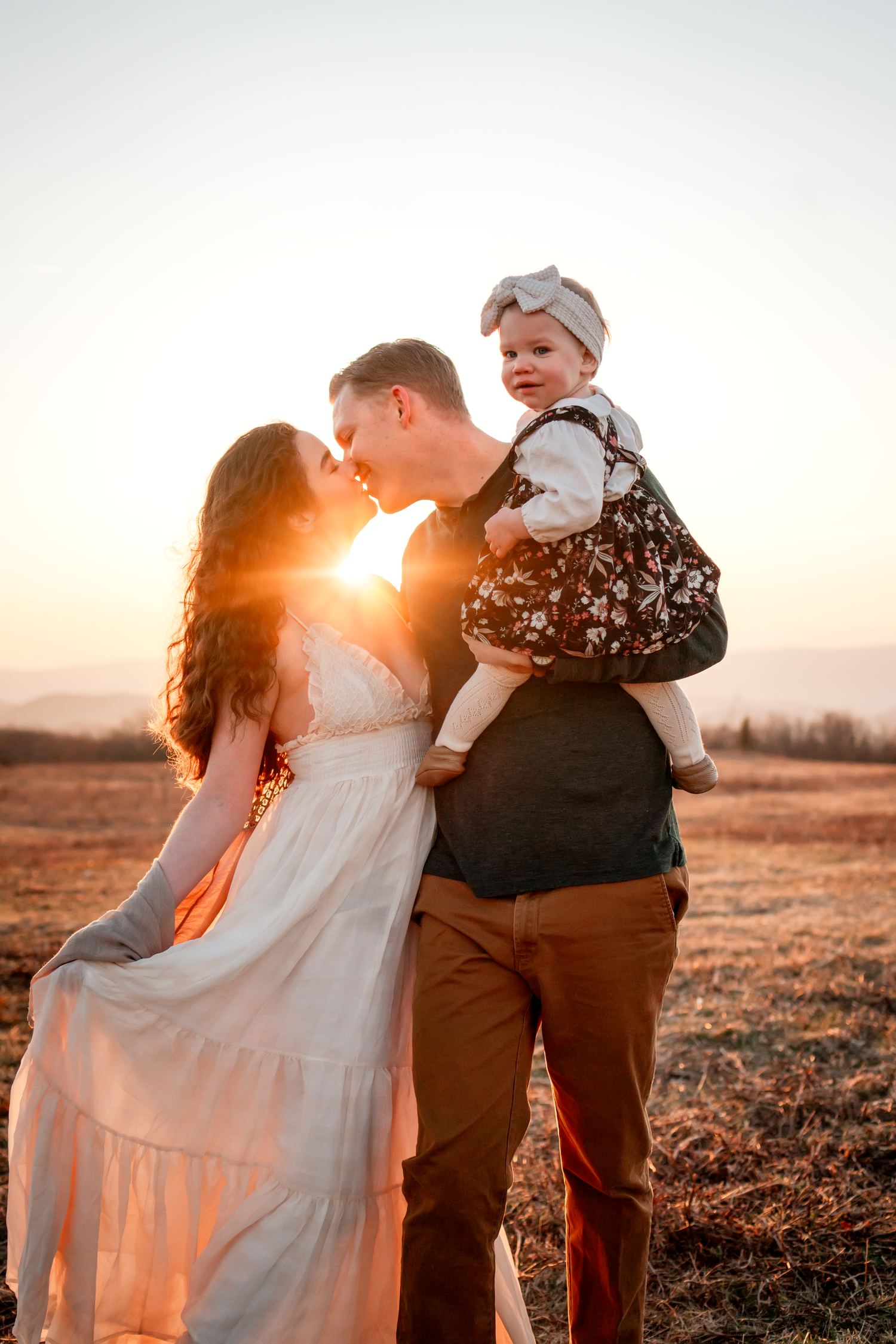 Family portrait silhouetted against a dramatic sunset in an open field.
