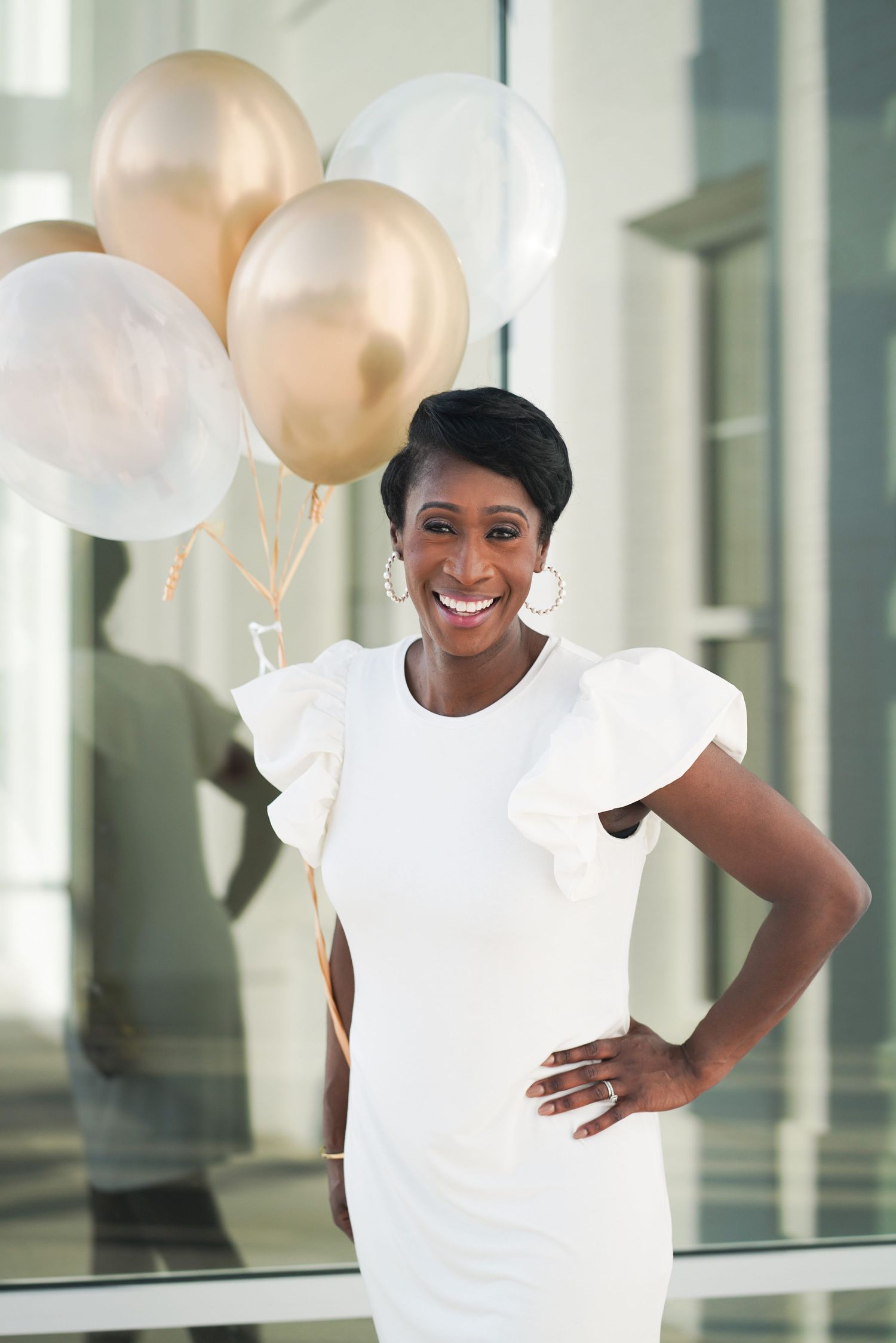 Elegant portrait in white dress with gold balloons in modern building interior.