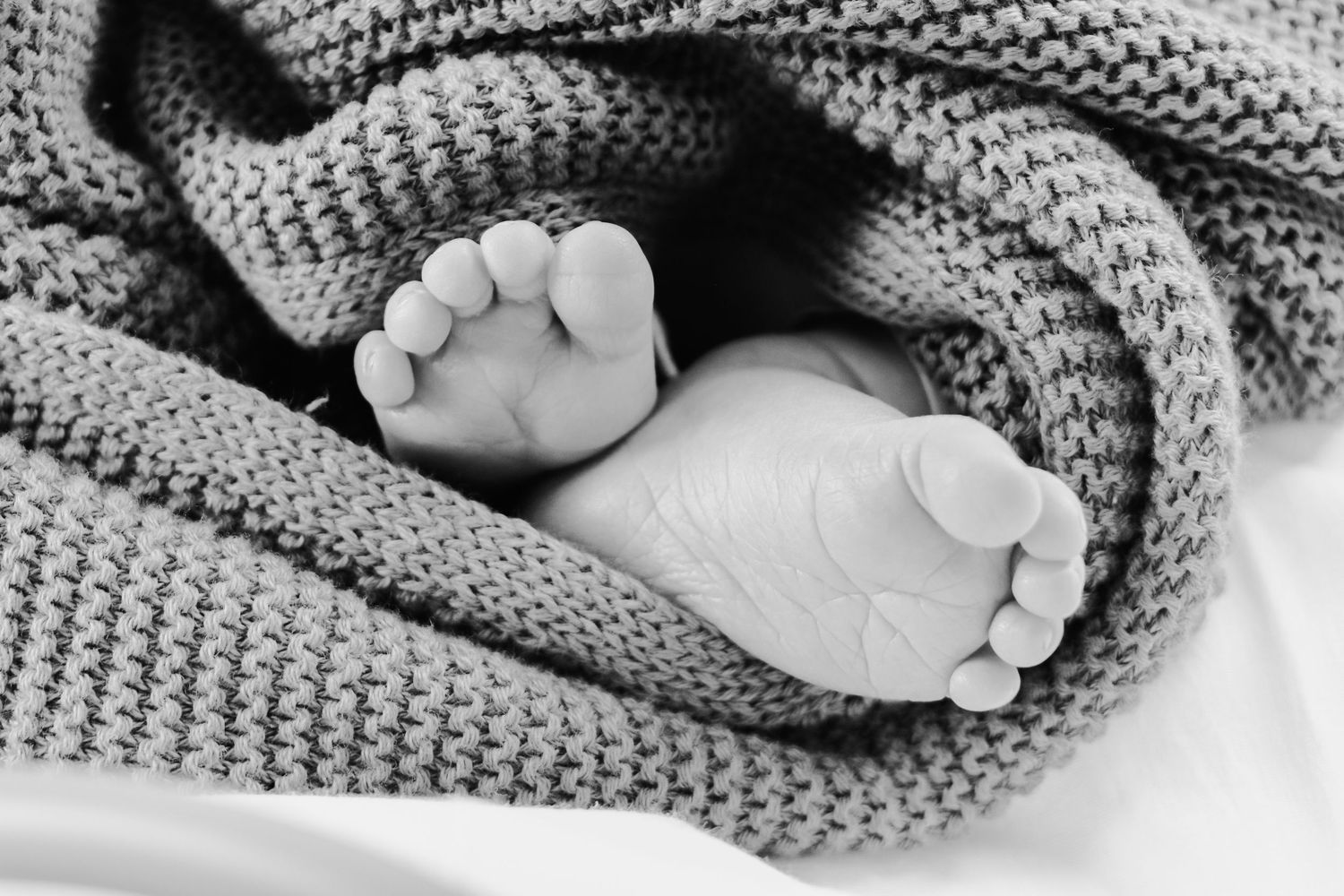 Black and white close-up of tiny newborn feet wrapped in knitted blanket.