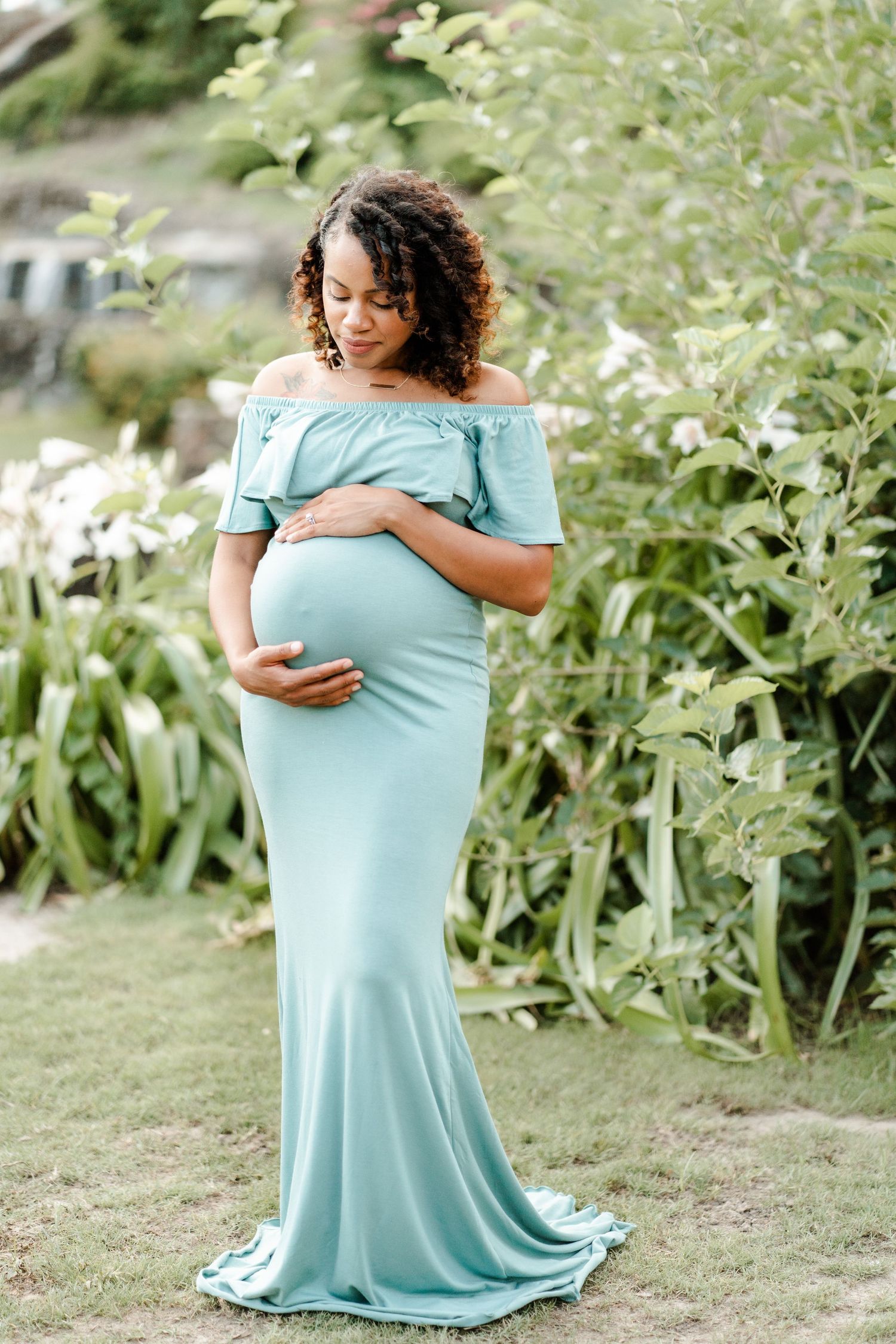 A person in a flowing mint green dress poses in front of lush greenery in a garden setting.