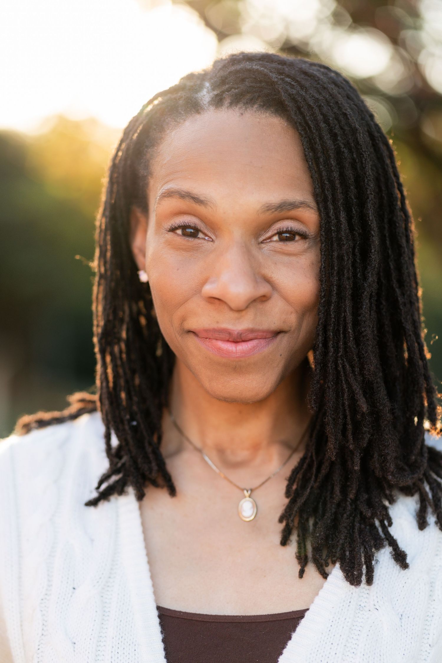 Portrait of someone with dreadlocks wearing a white top and smiling warmly at sunset.