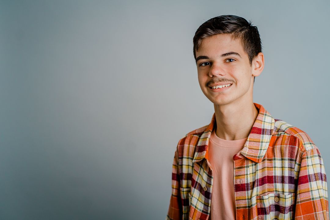 Young person in orange plaid shirt smiling and posing against a gray background in a photo series.