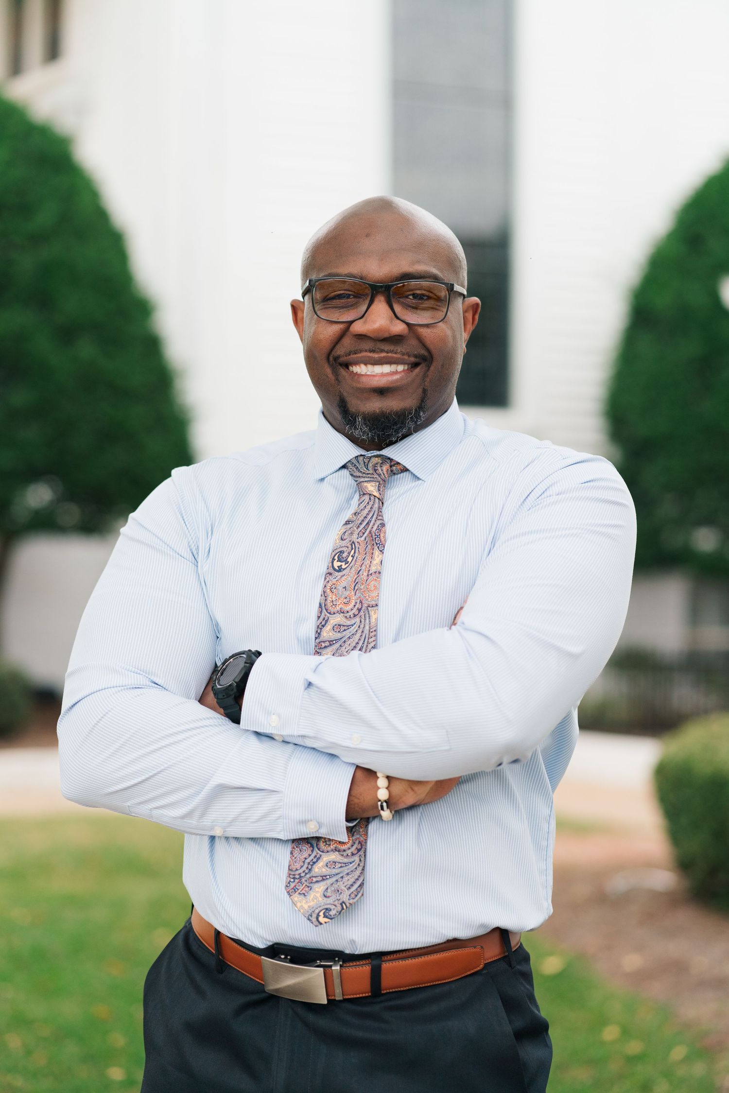 Professional wearing white dress shirt and patterned tie poses confidently with arms crossed.