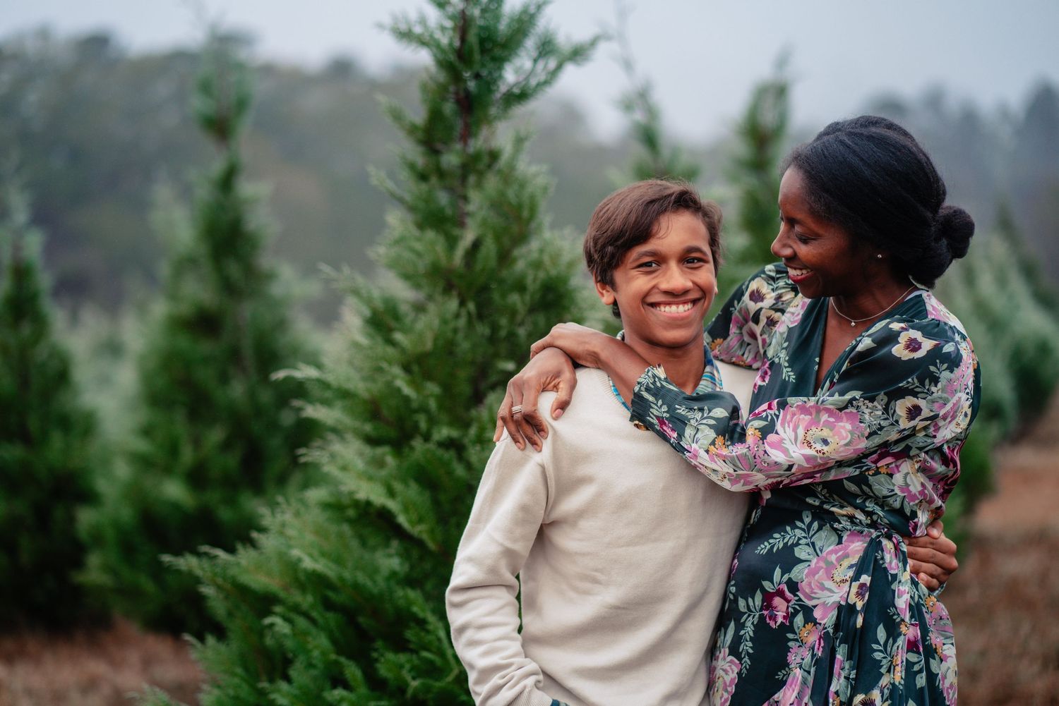 A couple shares joyful moments together in front of evergreen trees during an outdoor photo session.