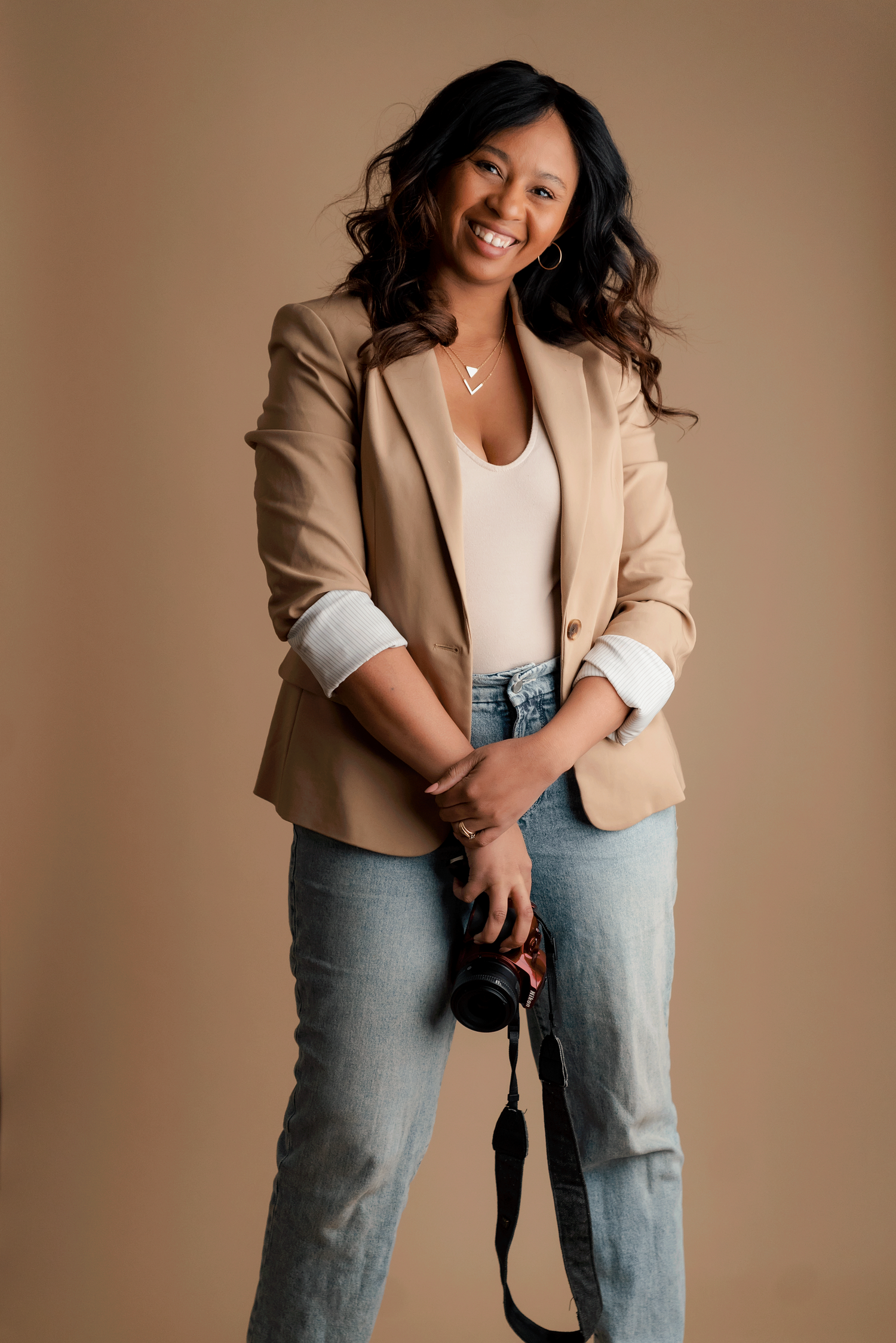 Professional studio portrait of someone wearing a beige blazer, white top and light wash jeans against a neutral background.