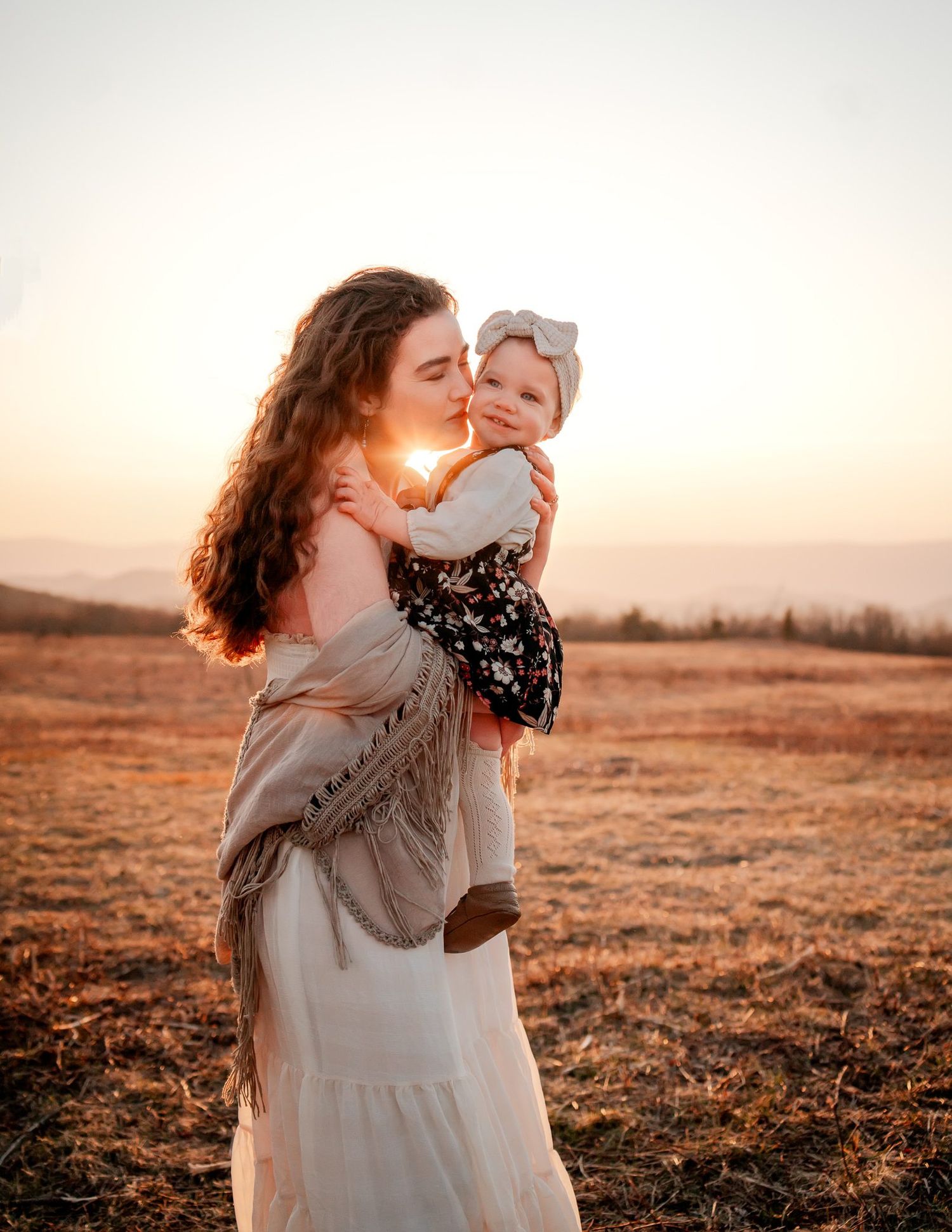Sweet maternal bonding moment captured at sunset in a golden field.