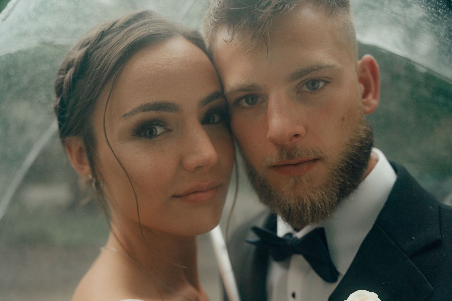 Close-up portrait of bride and groom sharing an intimate moment under a clear umbrella.