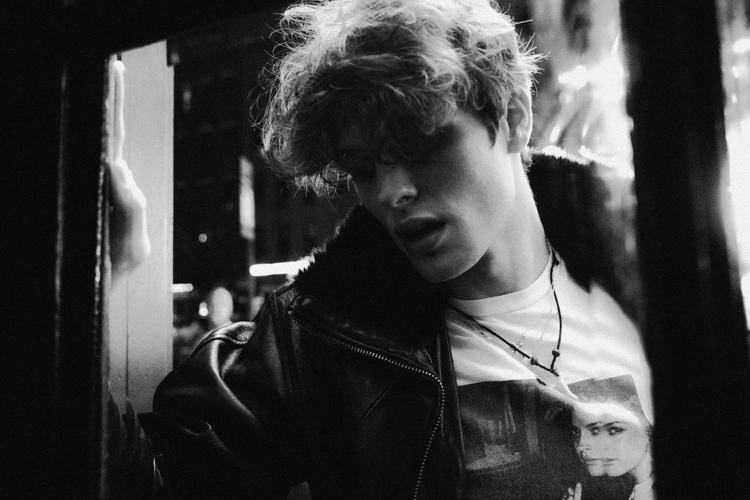 Black and white portrait of a young person in a leather jacket under dramatic lighting.