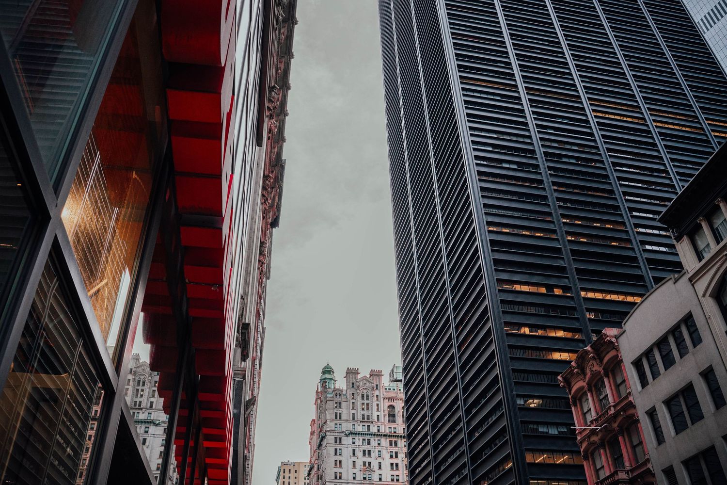 Low angle urban street view of contrasting red and dark glass skyscrapers in city canyon.