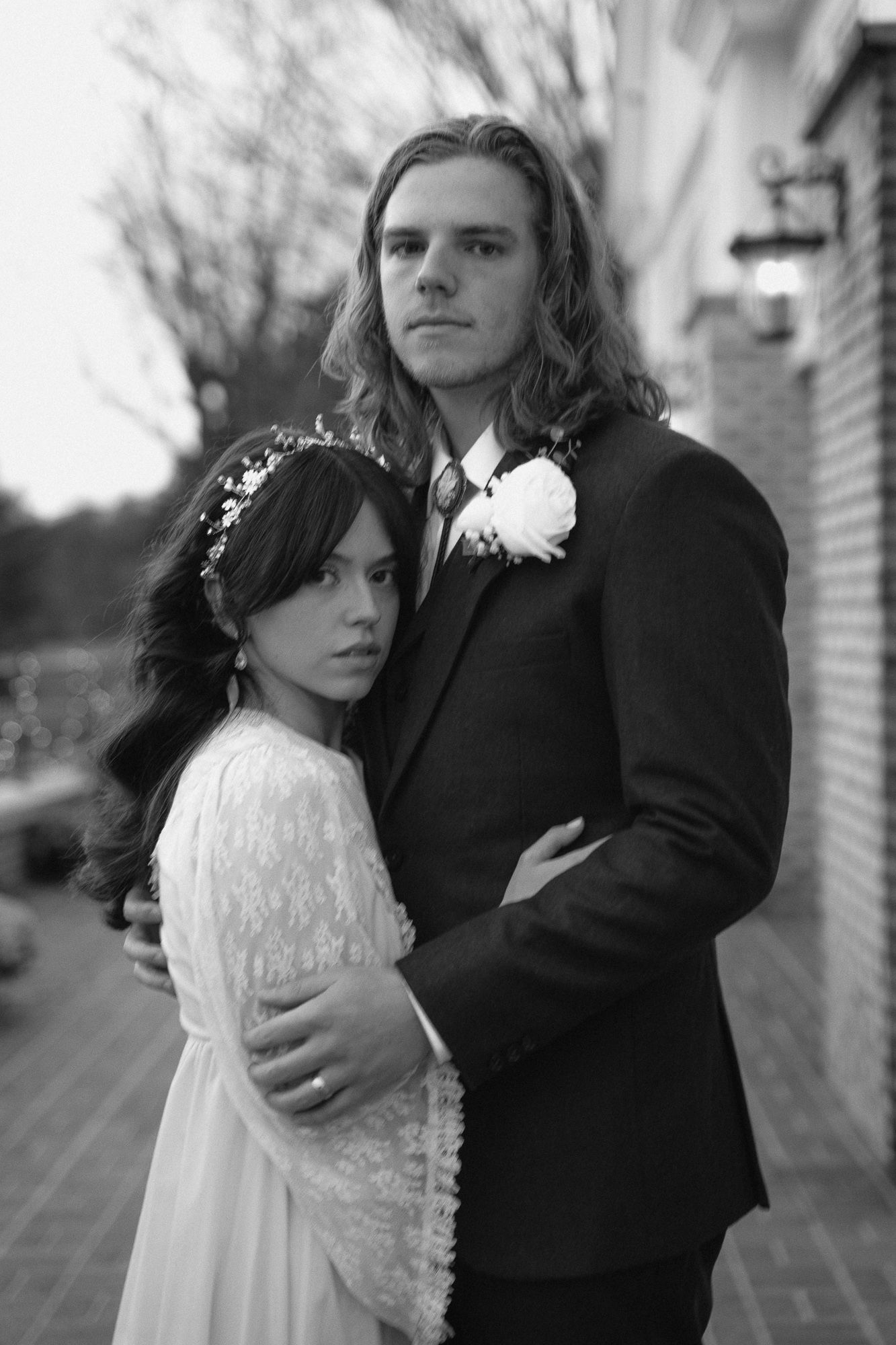 Black and white portrait of bride and groom embracing outdoors in wedding attire with boutonniere.