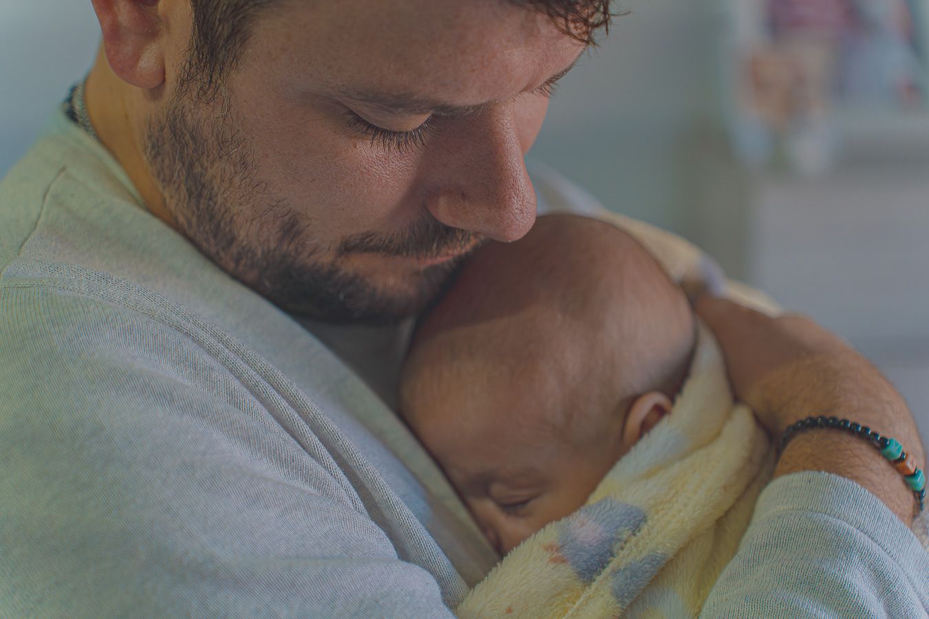 Papá abrazando y consolando a su bebé recién nacido junto a la ventana, sesión de fotos newborn lifestyle a domicilio en Barcelona, Meraki