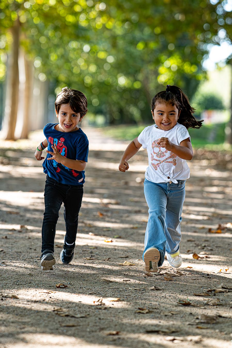 Dos niños pequeños corriendo felices por un camino de tierra entre los árboles, reportaje de fotos familiar en exteriores en Sant Cugat,