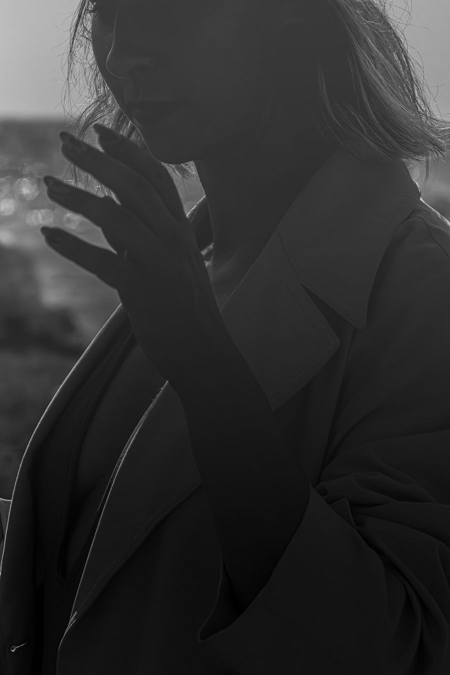 Dramática silueta en blanco y negro de una persona con abrigo y el pelo al viento contra una brillante luz de fondo.