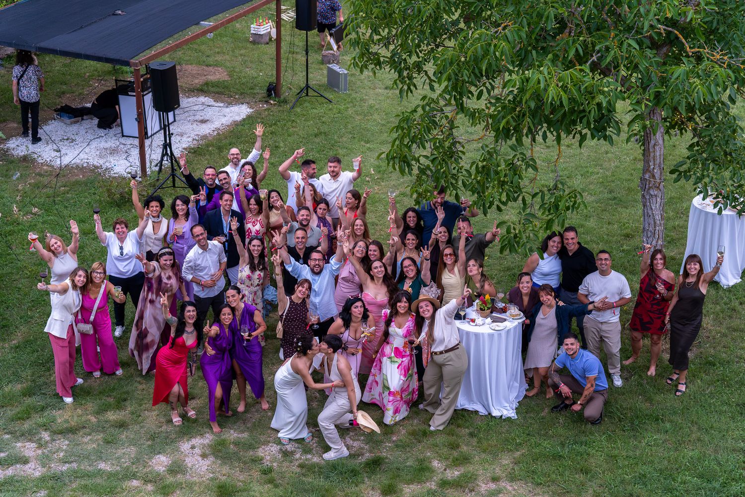 Large group of joyful guests posing together outdoors at a garden party or wedding celebration.