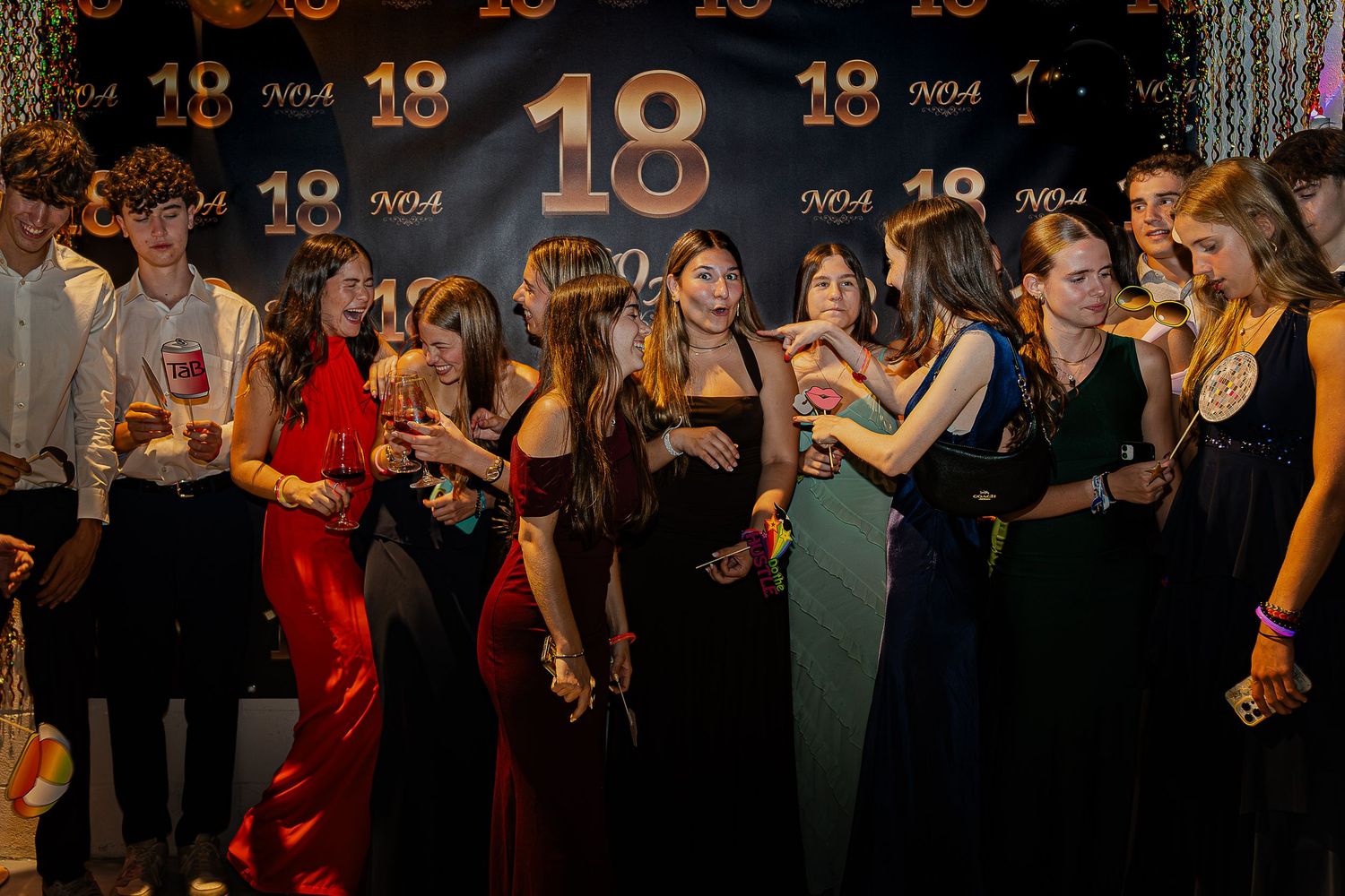 Teens celebrate an 18th birthday party, posing in formal attire against a gold and black backdrop.
