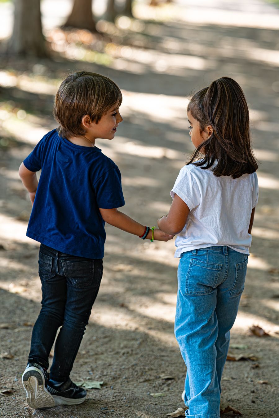 Dos niños cogidos de la mano mientras están de pie en un camino de tierra bajo la luz del sol moteada.