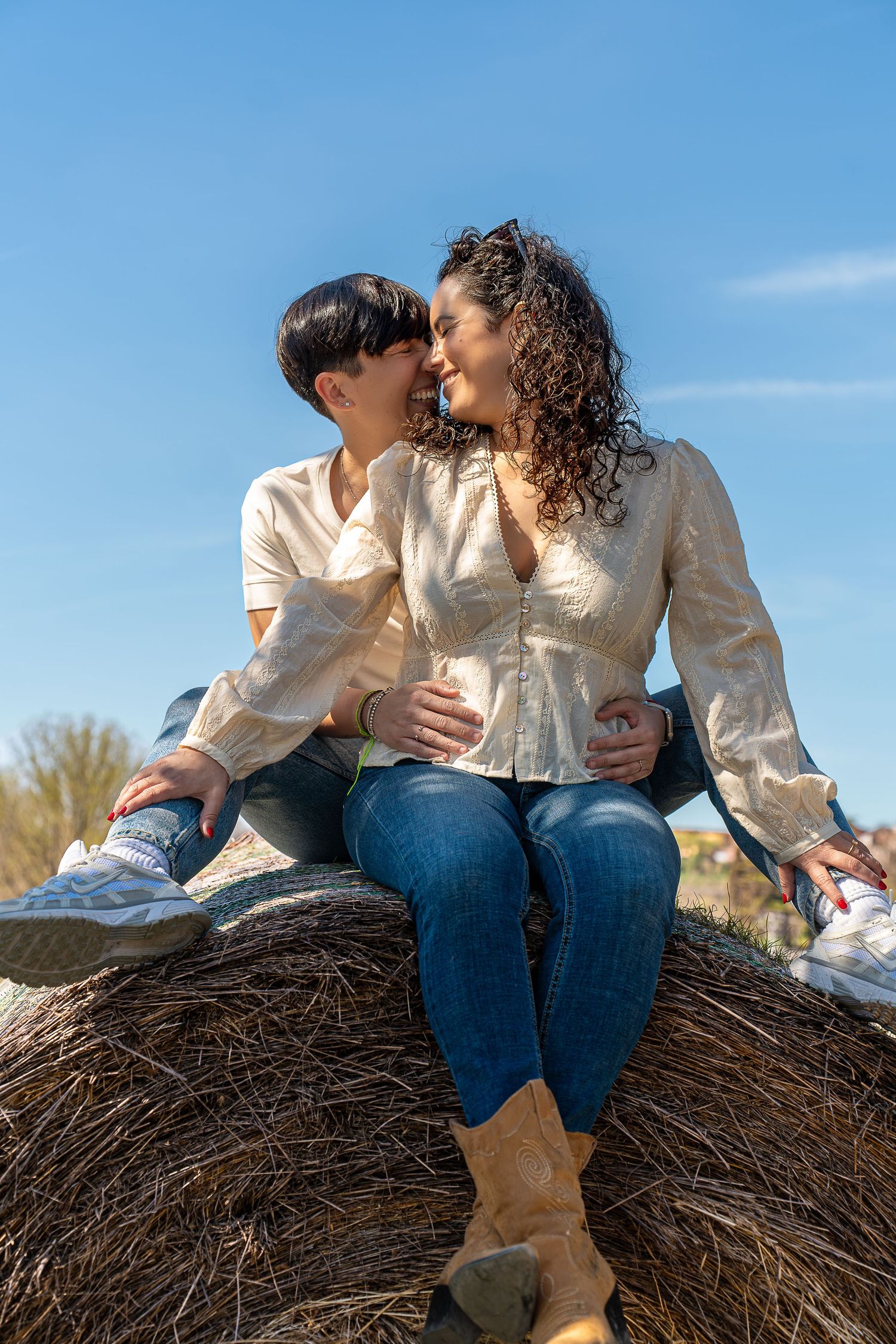 Pareja de mujeres en una bala de paja compartiendo un momento romántico. Fotografía preboda inclusiva al aire libre en Barcelona.