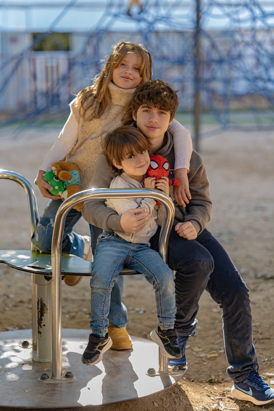 Tres hermanos sentadas juntas en un tiovivo en ropa informal en un día soleado en un parque.